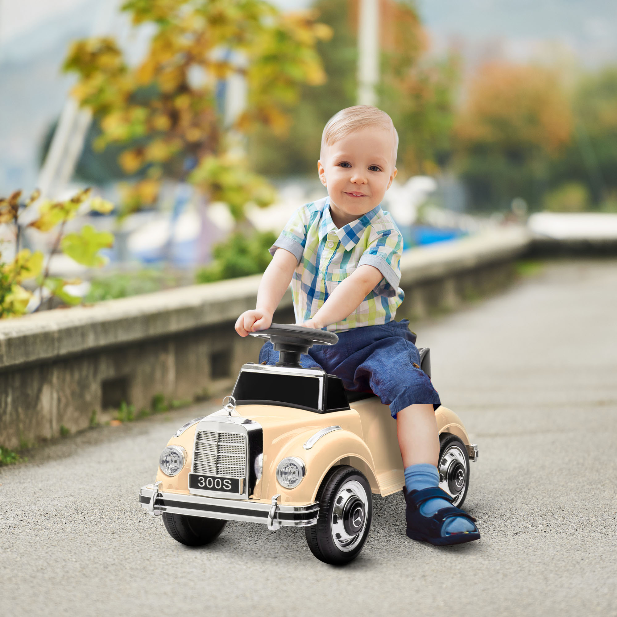 Un bambino è seduto in un'auto giocattolo beige classica, sorridendo. Lo sfondo è una strada pavimentata.