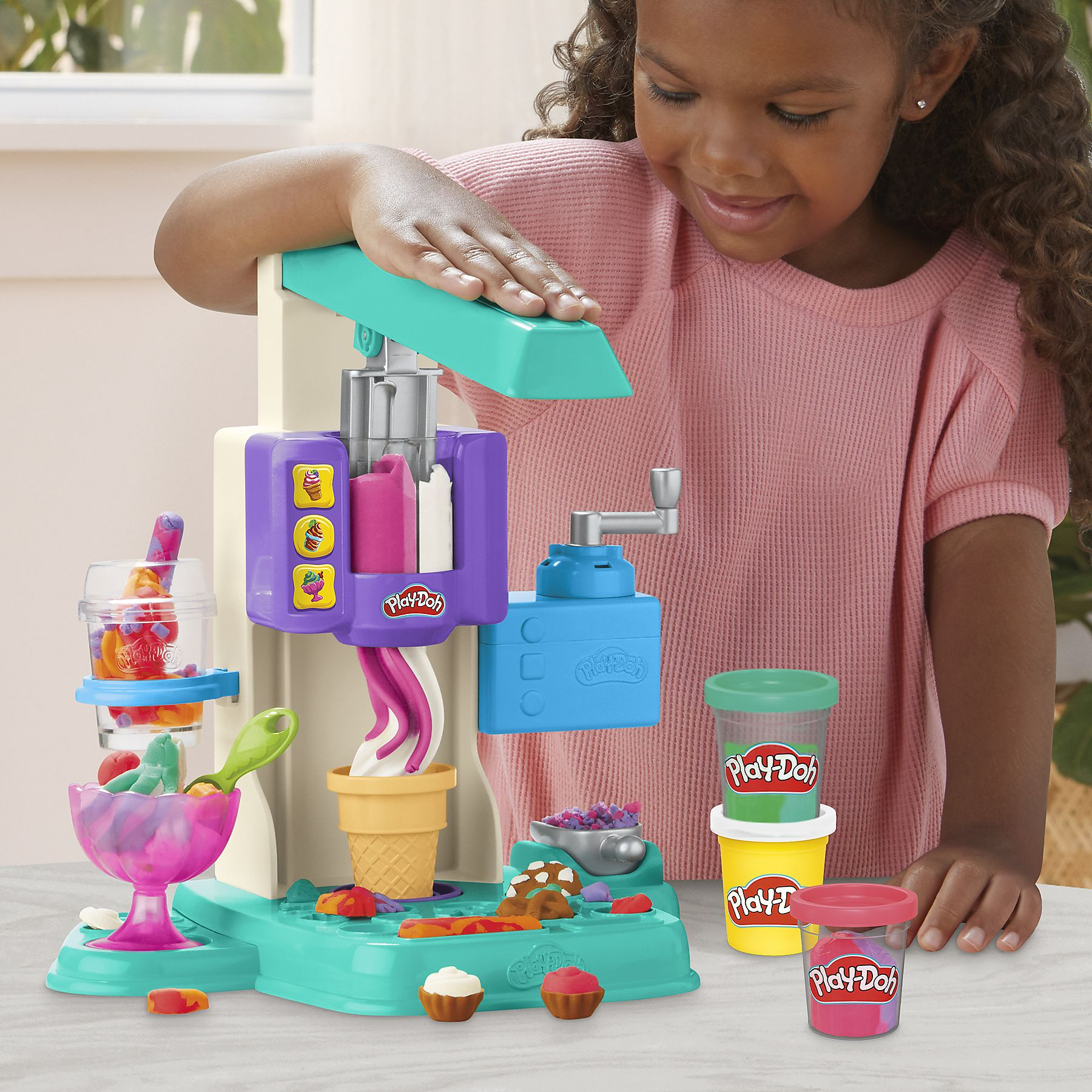 Un bambino usa una macchina per gelati Play-Doh. Play-Doh colorato e gelato sono sul tavolo.
