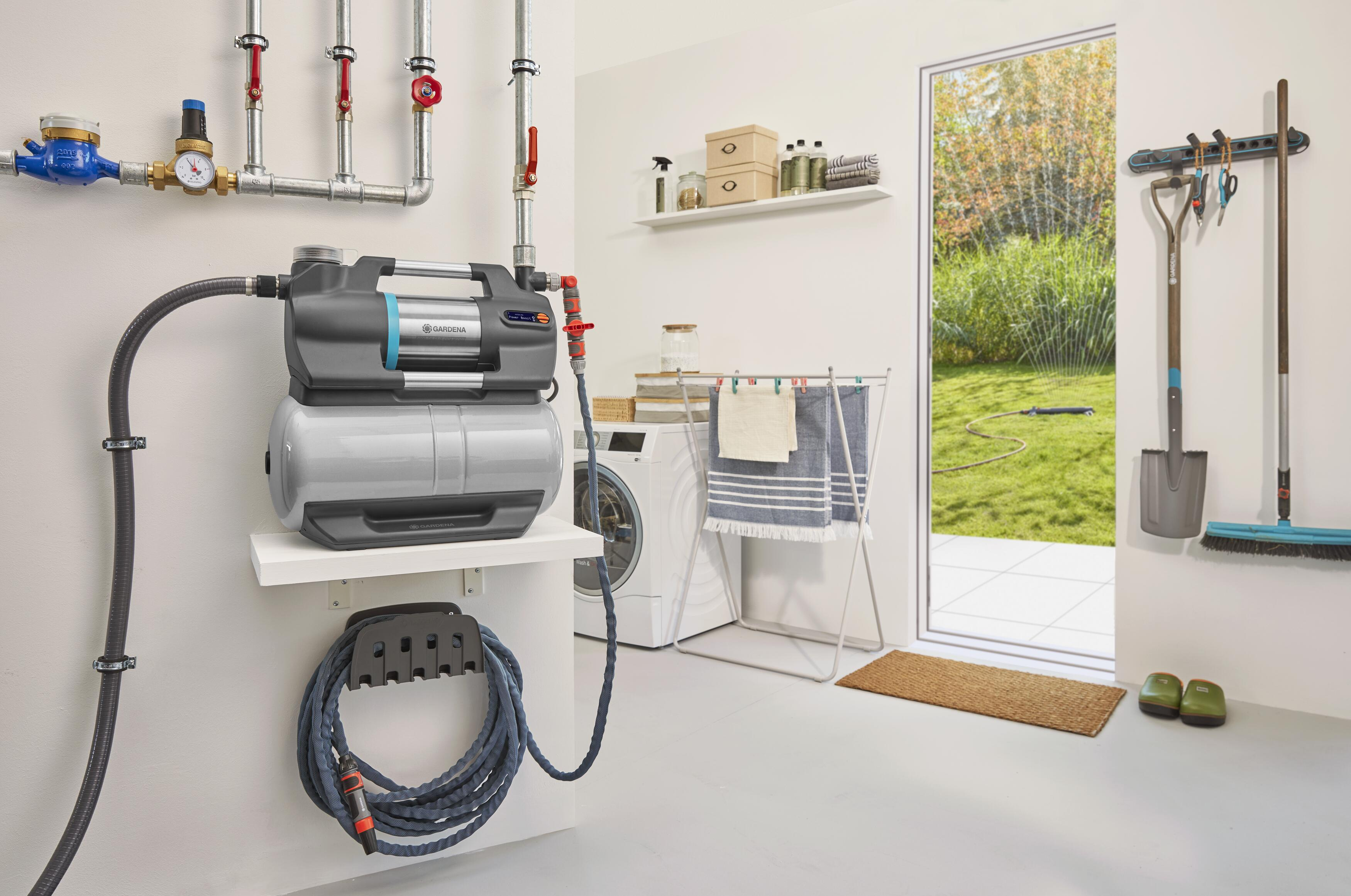 Ein weißer Hauswirtschaftsraum mit einem Wasserpumpensystem und Gartengeräten an der Wand.