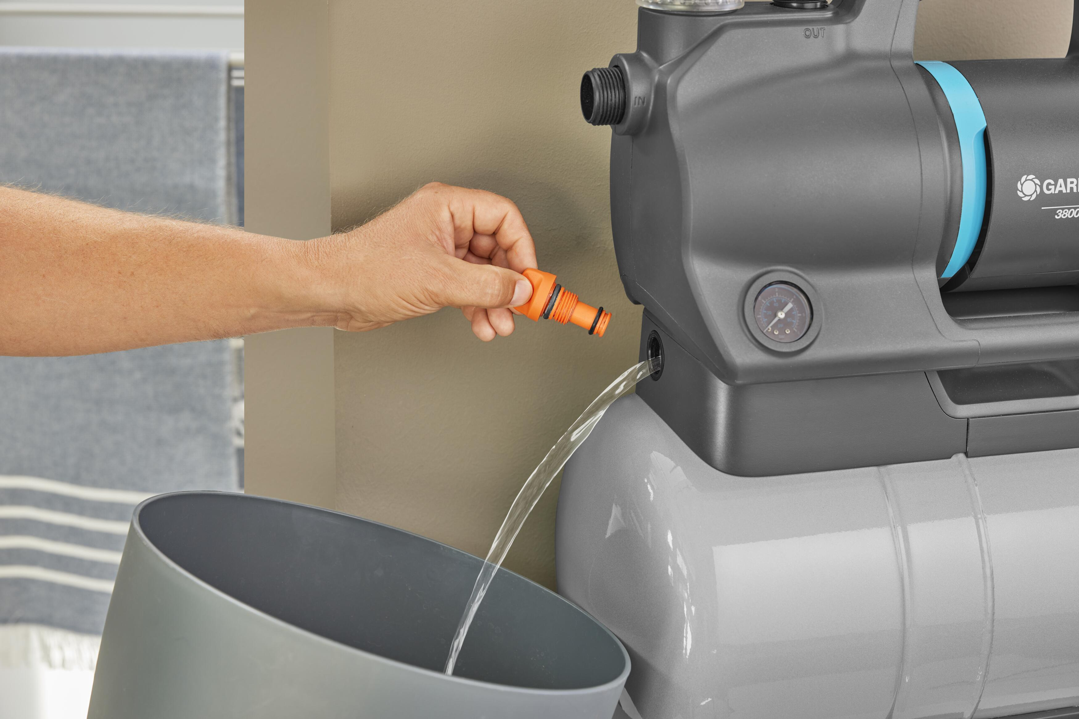 Eine Person gießt Wasser aus einer Pumpe in einen grauen Eimer. Die Pumpe ist grau und orange.