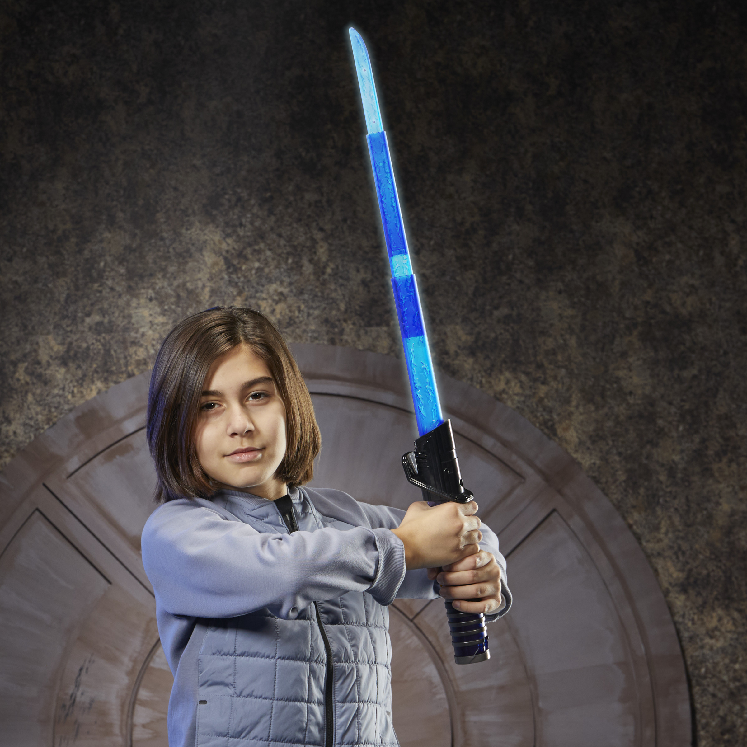 Dziecko trzymające niebieski miecz świetlny i ubrane w szarą kurtkę.