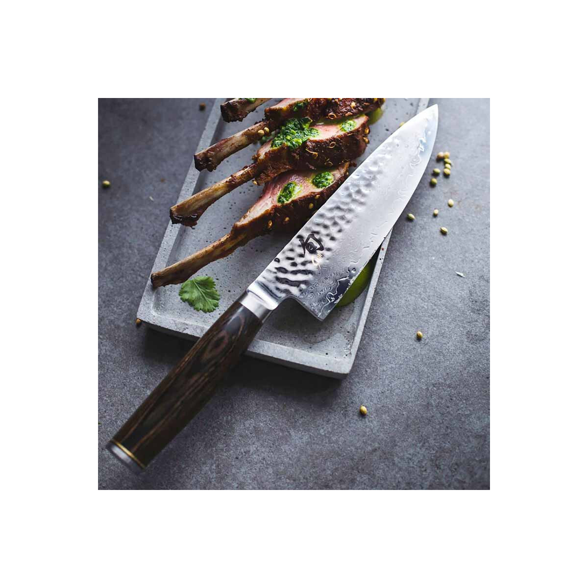 Un coltello accanto a carne cotta su un vassoio con erbe, posto su una superficie grigia.