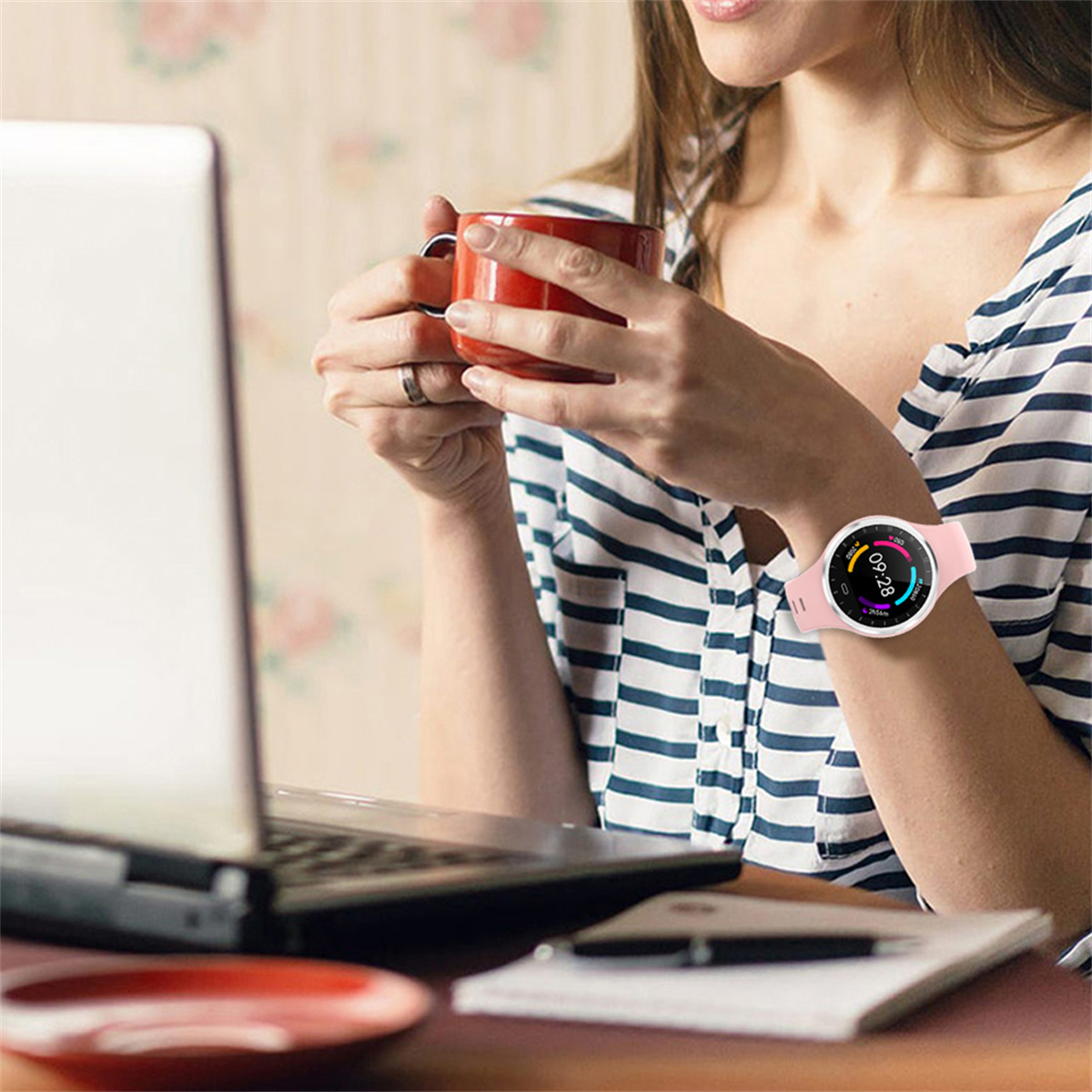 Frau mit rosa Smartwatch, Laptopnutzung, roter Becher.