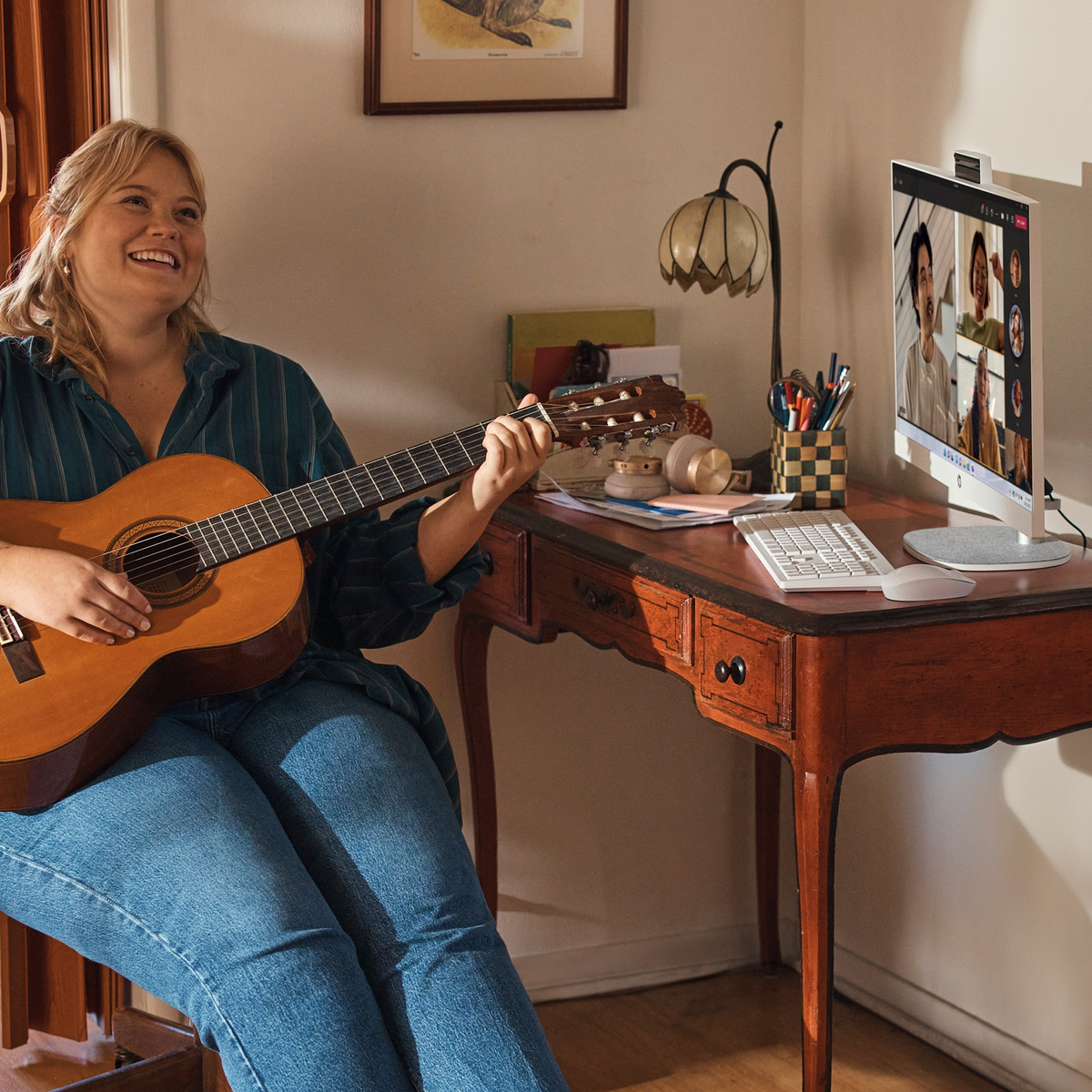 Kobieta gra na gitarze i uśmiecha się, rozmowa wideo na ekranie komputera, konfiguracja domowego biura.