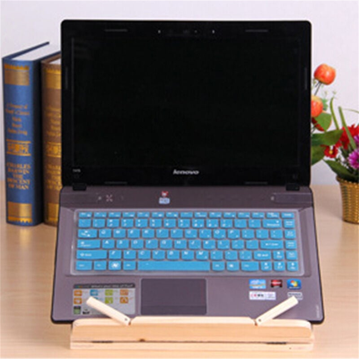 Laptop auf Holzständer, blaue Tastaturabdeckung, Bücher.