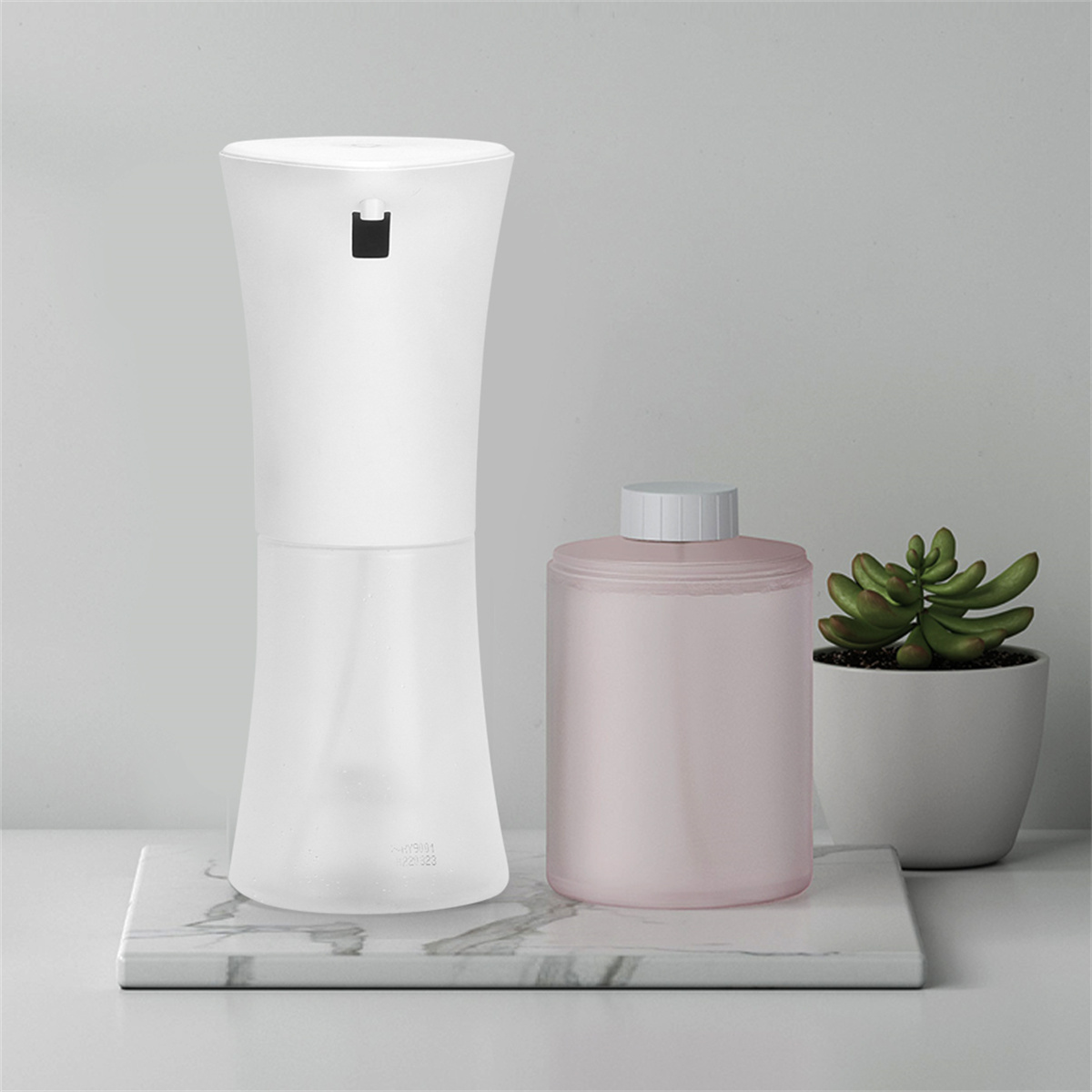 Weißer automatischer Seifenspender und rosa Nachfüllflasche auf Marmoroberfläche.