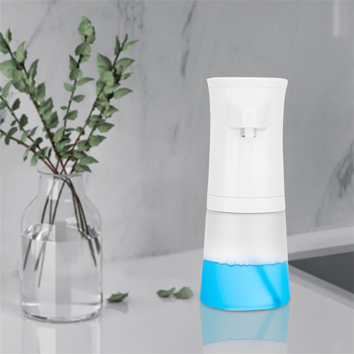 Ein weißer automatischer Seifenspender mit blauer Flüssigkeit und eine Glasvase mit Grün.