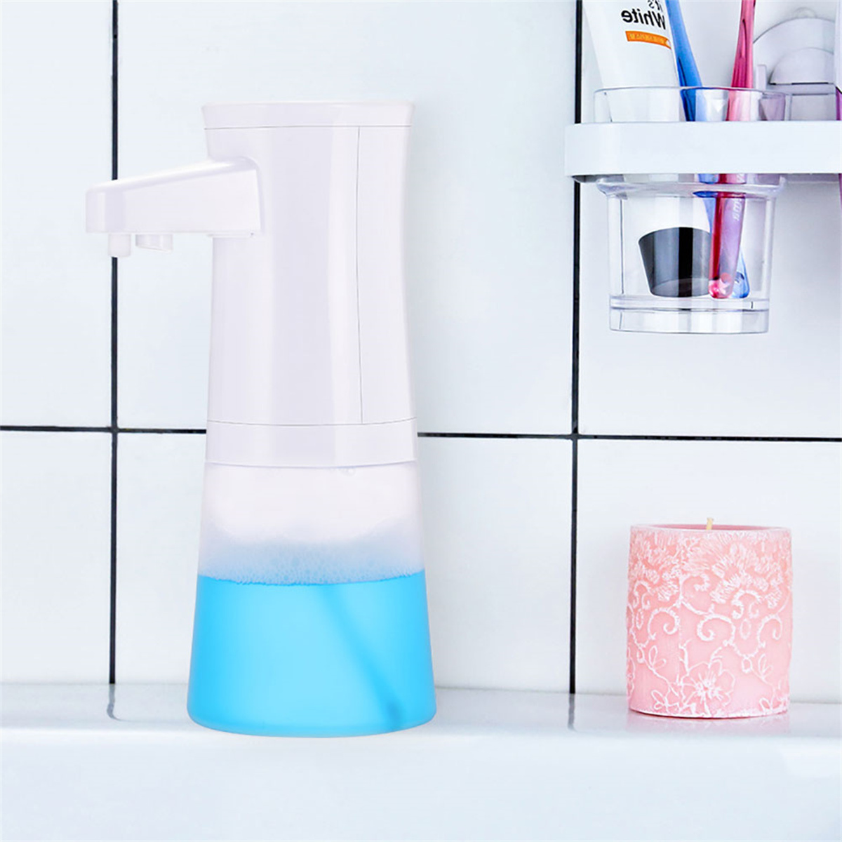 Ein weißer Seifenspender mit blauer Flüssigkeit und eine rosa Kerze. Der Hintergrund ist eine geflieste Wand.