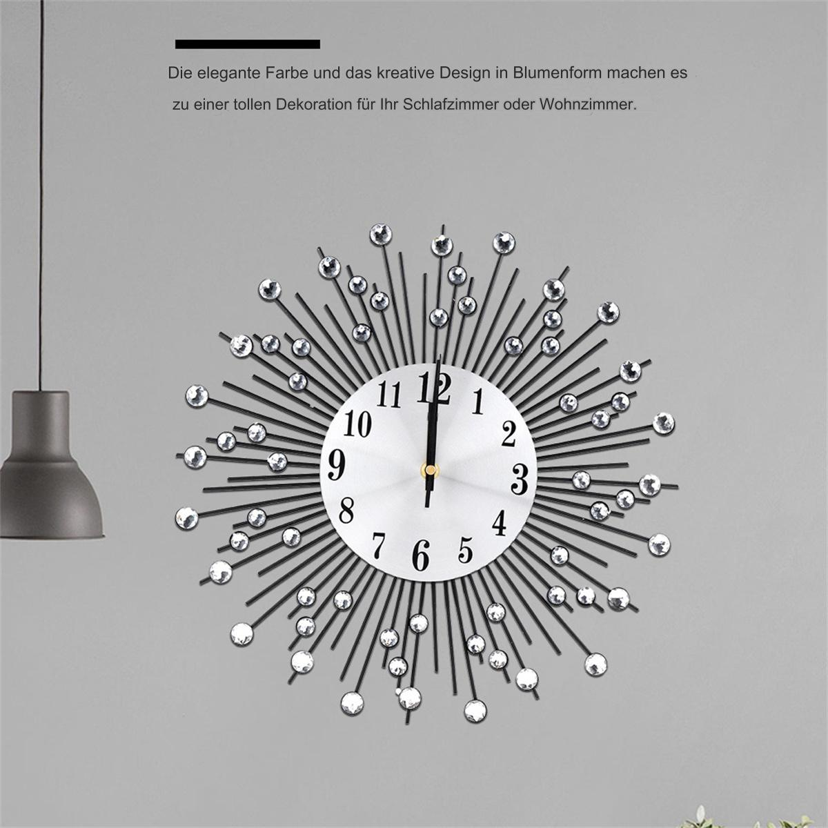 Eine dekorative Uhr vor einer grauen Wand. Sie hat ein Sonnenstrahl-Design mit Kristallen.