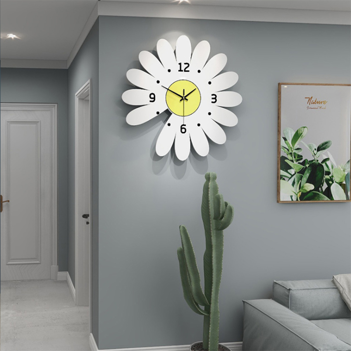 Weiße Gänseblümchen-Uhr an einer grauen Wand, mit einem Kaktus und einem Gemälde.