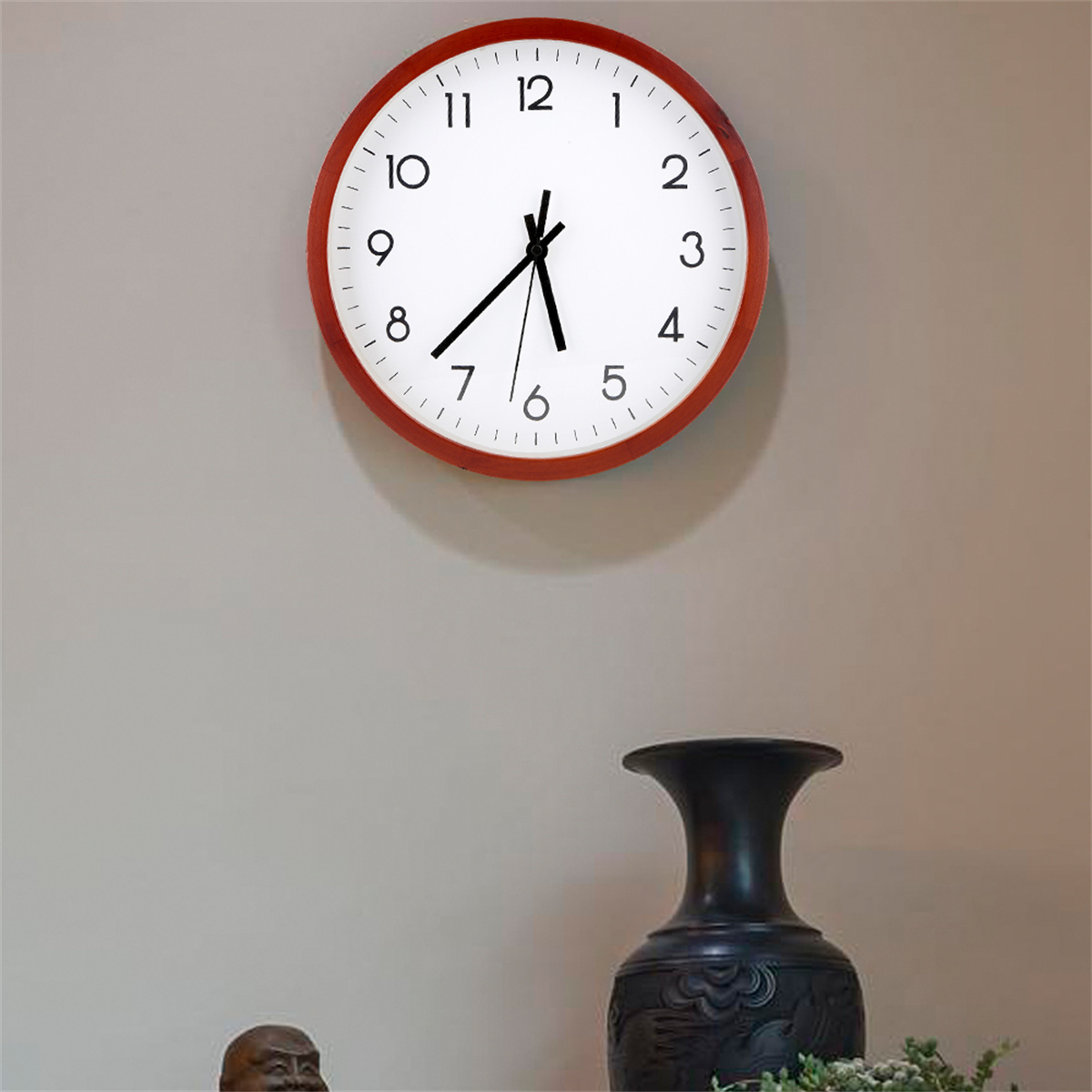 Runde Wanduhr mit rotem Rahmen, weißem Zifferblatt, schwarze Zahlen. Vase unten.