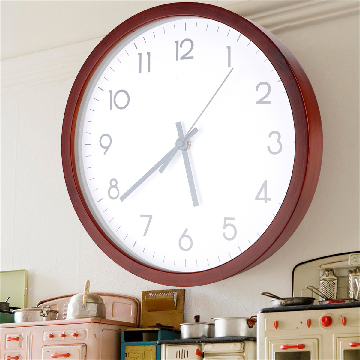 Eine große, runde Uhr an einer weißen Wand. Die Uhr hat einen dunklen Holzrahmen und ein weißes Zifferblatt mit schwarzen Zahlen.