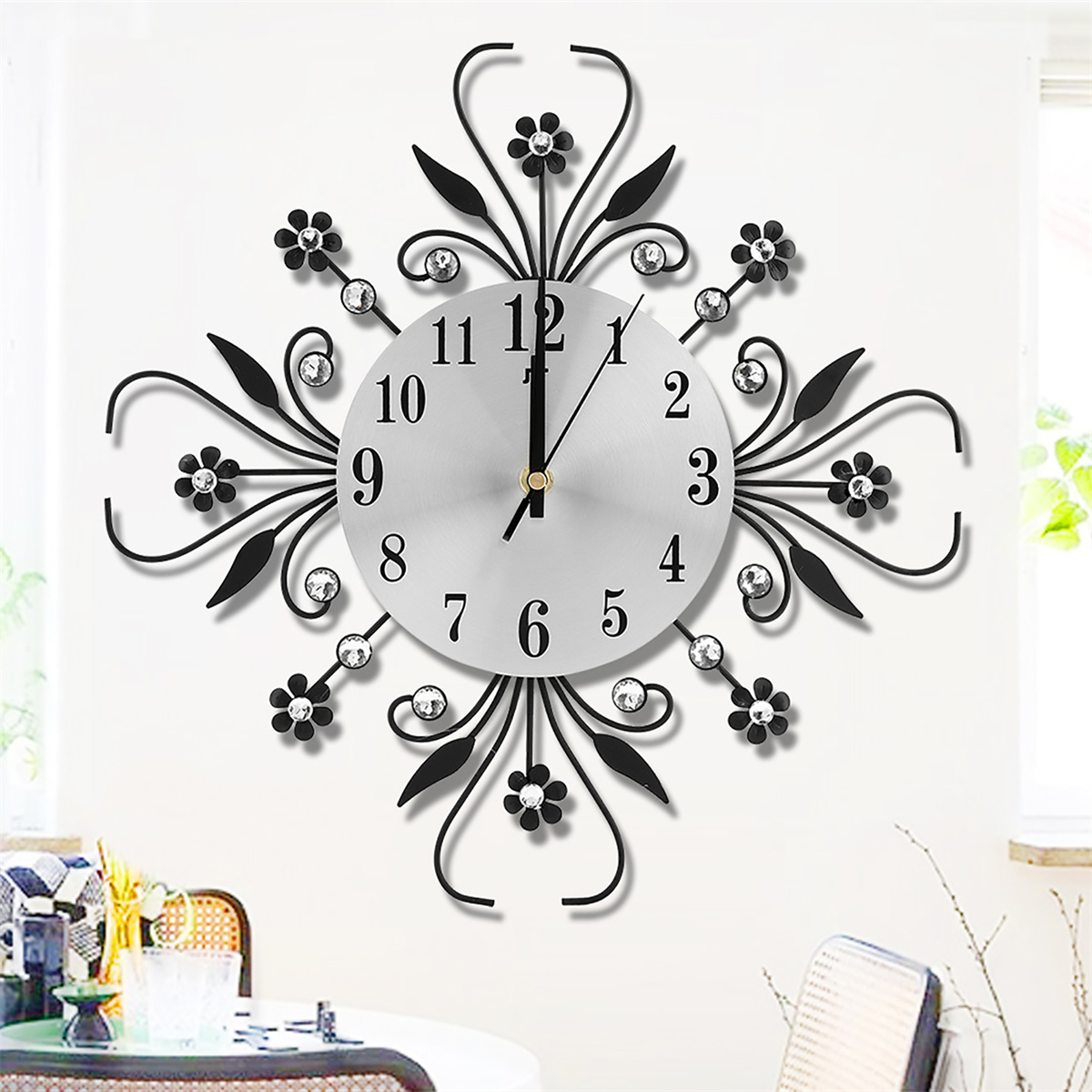 Eine silberne Uhr mit schwarzem, kunstvollem Blumendesign und Kristallen; Zeiger zeigen auf 7:00 Uhr.