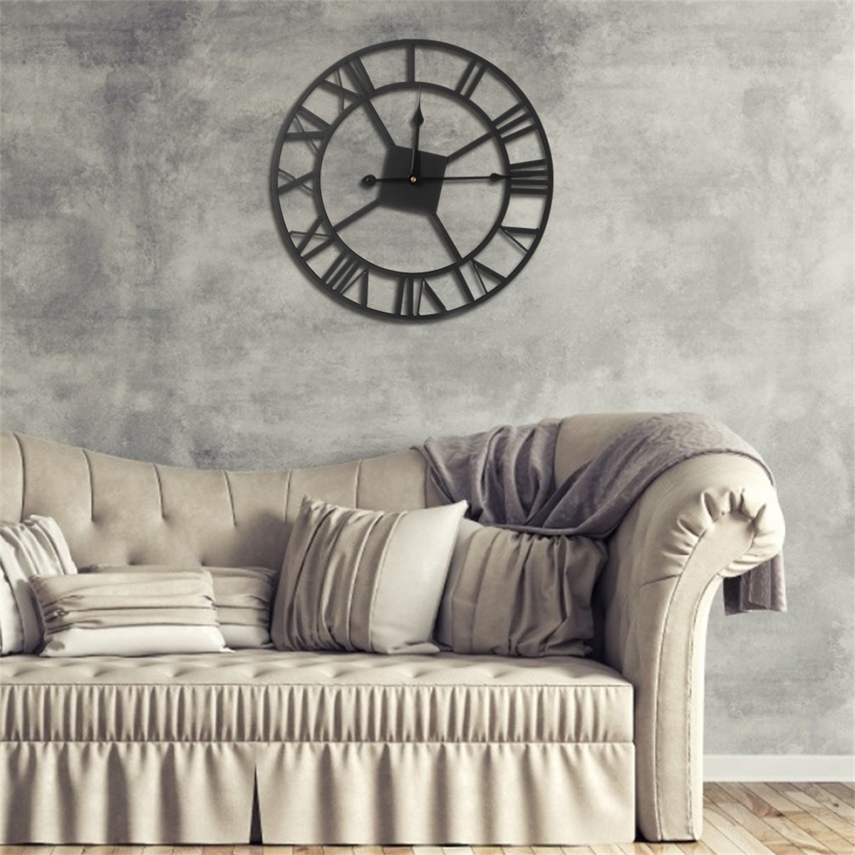Schwarze Metall-Wanduhr, römische Ziffern, an grauer Wand. Beiges Sofa mit Kissen.