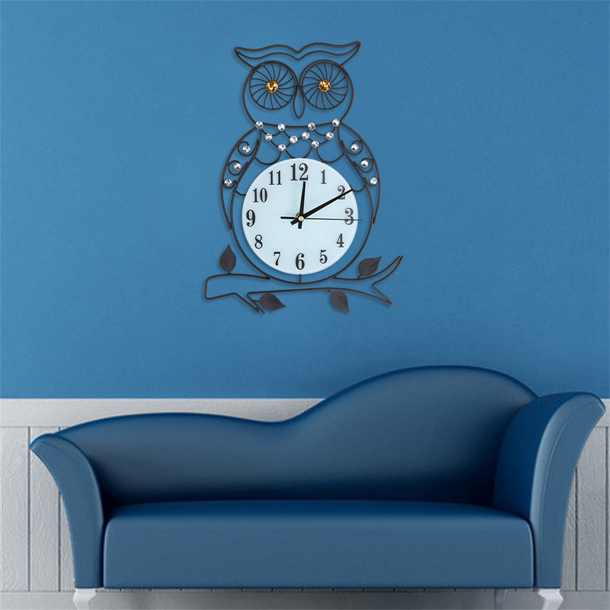 Eine Eule-Uhr an einer blauen Wand über einem blauen Sofa. Die Uhr ist schwarz, weiß und hat goldene Details.