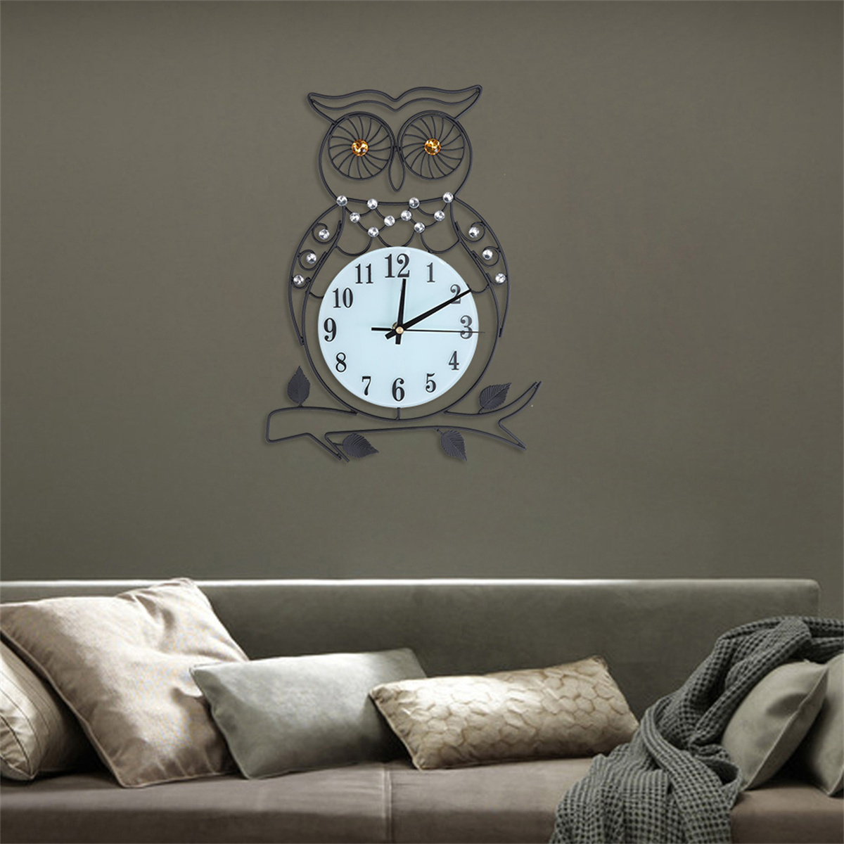 Eine eulenformige Uhr aus schwarzem Metall, die an einer Wand über einem Sofa hängt.