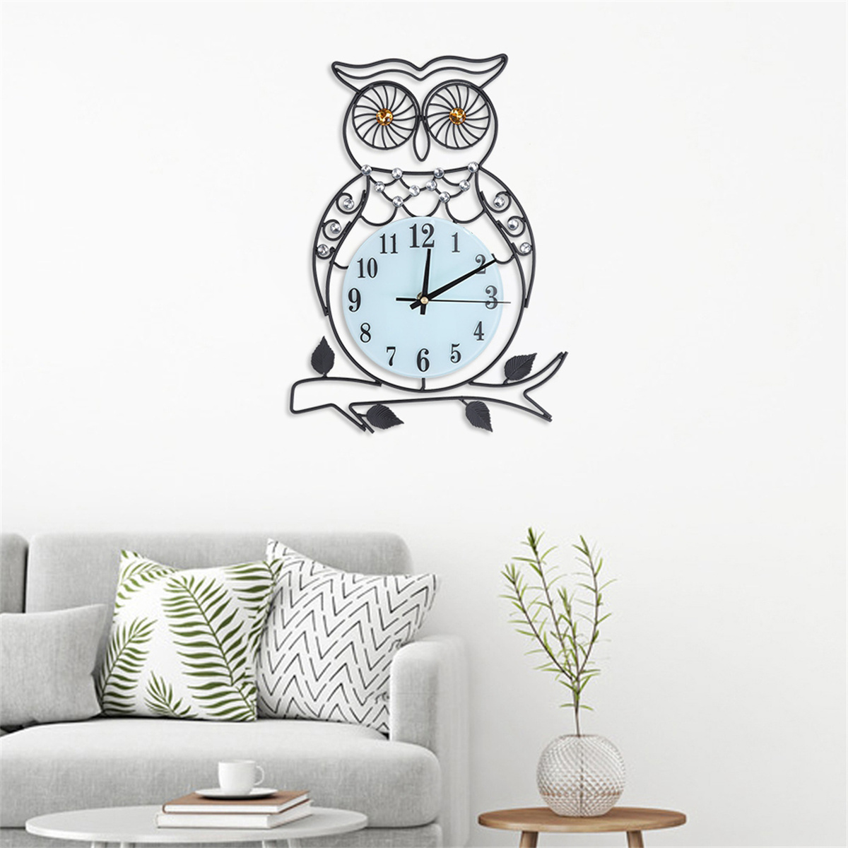 Eine eulenformige Uhr hängt an einer Wand. Darunter ein Sofa und eine Pflanze. Das Zifferblatt ist hellblau.
