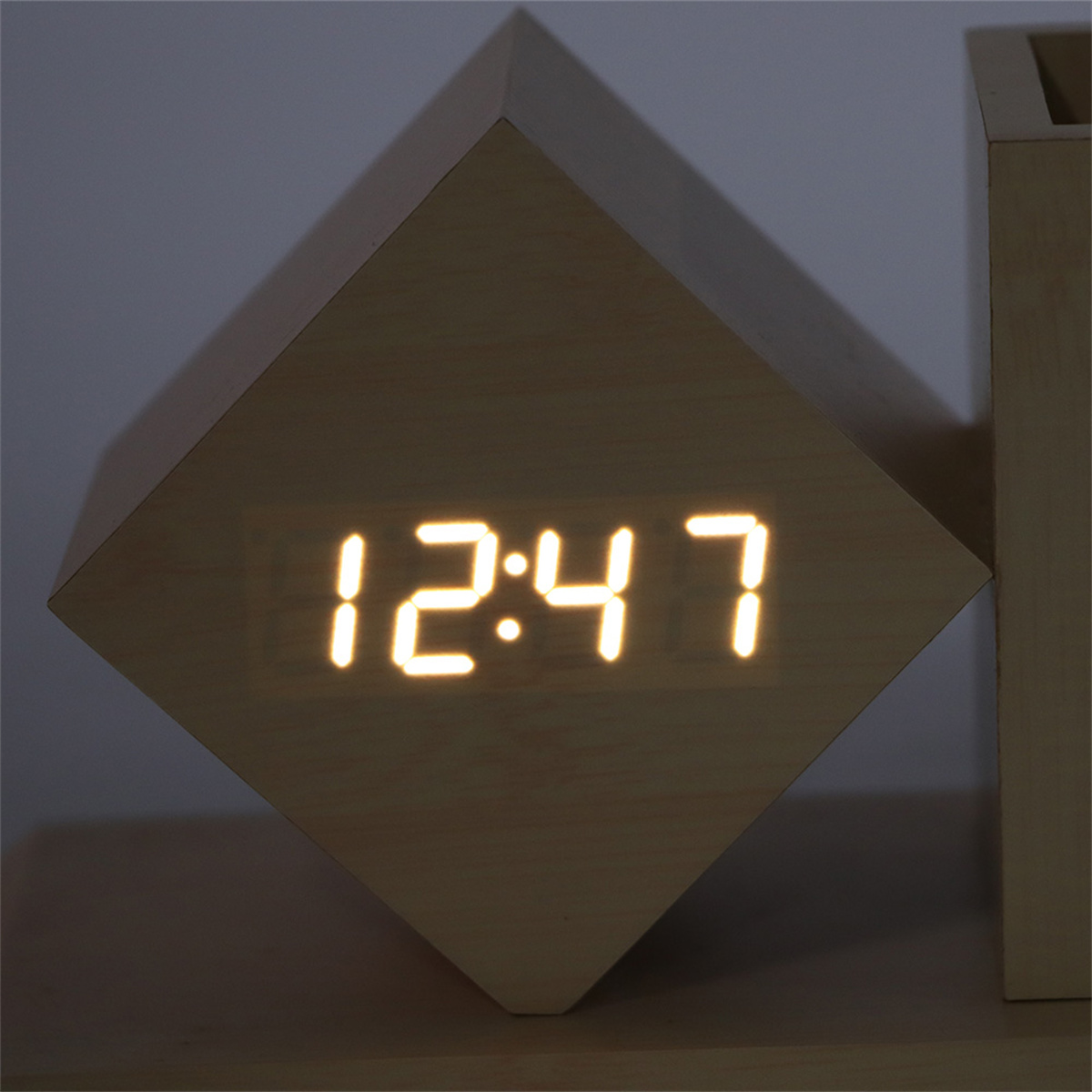 Würfelförmige Holzuhr mit Digitalanzeige 12:47. Beige Holzfarbe. Anzeige leuchtet.