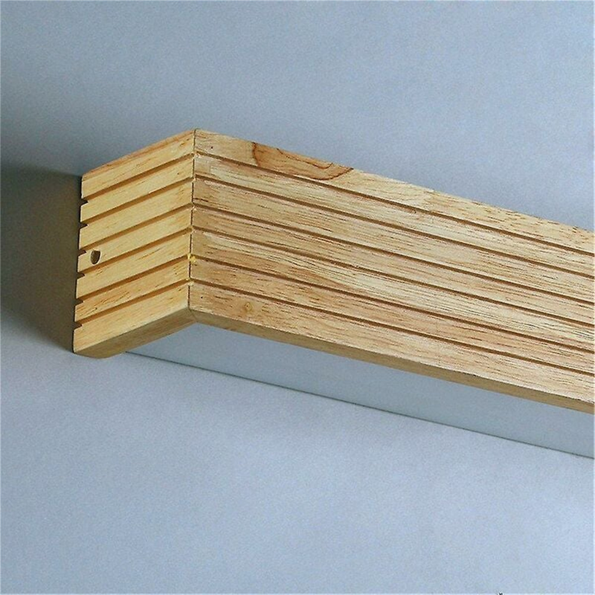 Ein hölzernes Eckstück mit horizontalen Rillen, das an einer weißen Wand befestigt ist. Die Ecke ist hellbraun.