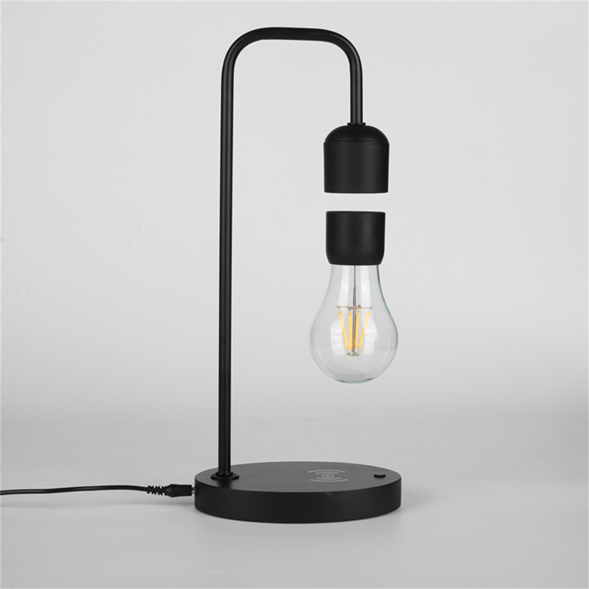 Schwarze schwebende Lampe mit einer Glühbirne, die in der Luft hängt. Sie hat einen gebogenen Arm und einen runden Sockel.