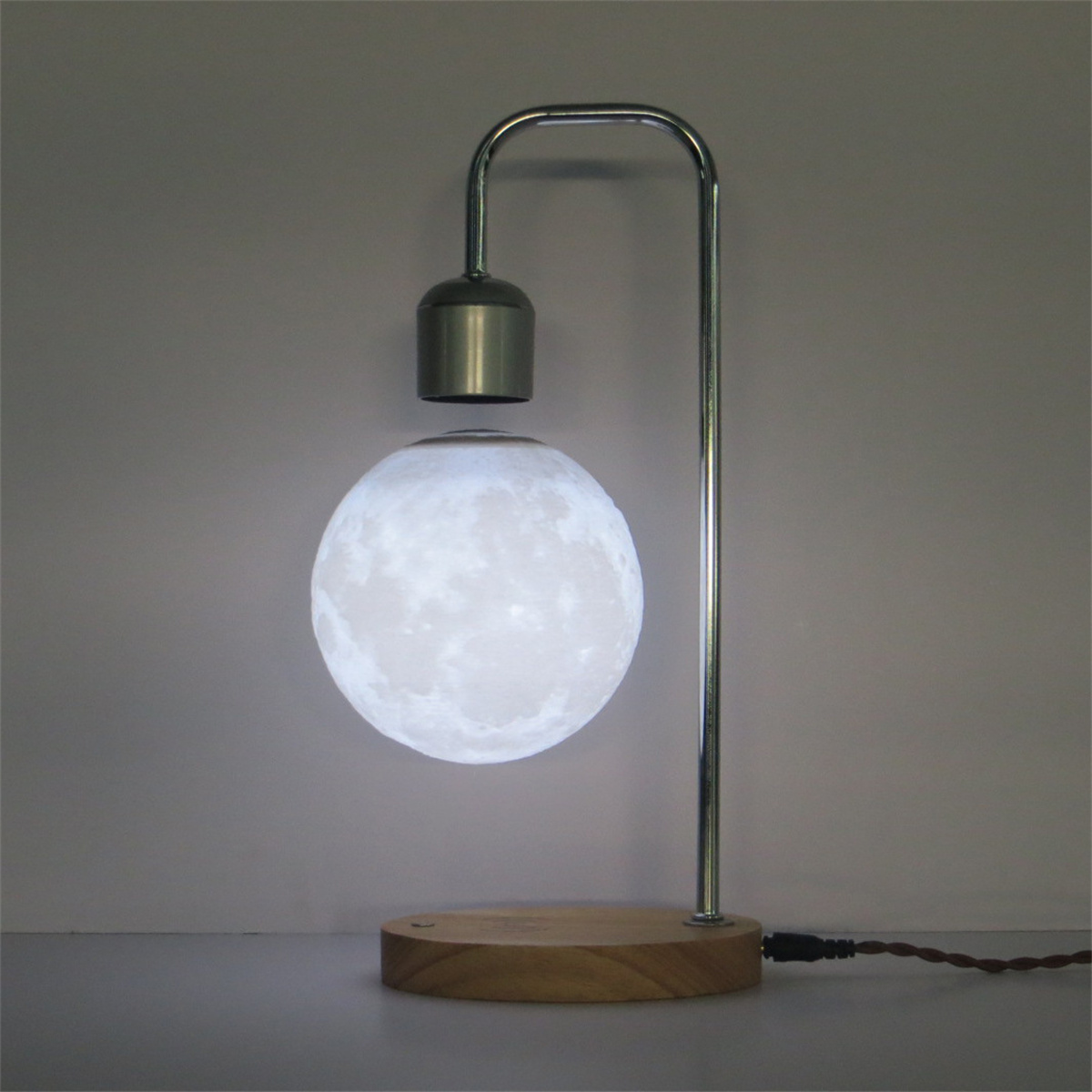 Eine mondförmige Lampe leuchtet, in der Luft hängend durch einen Metallständer auf einem Holzsockel.