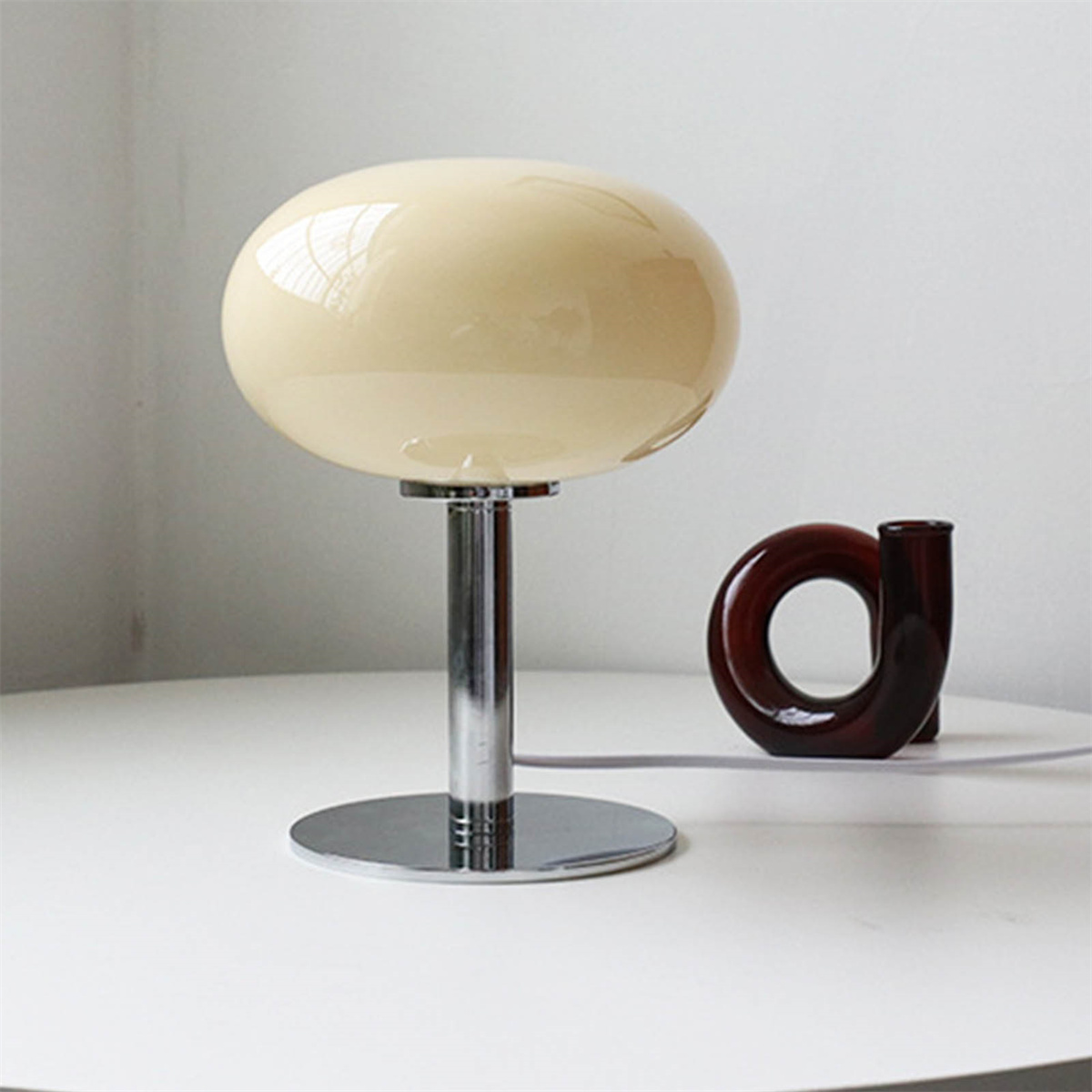 Eine cremefarbene, pilzförmige Lampe und eine braune Vase auf weißer Oberfläche.