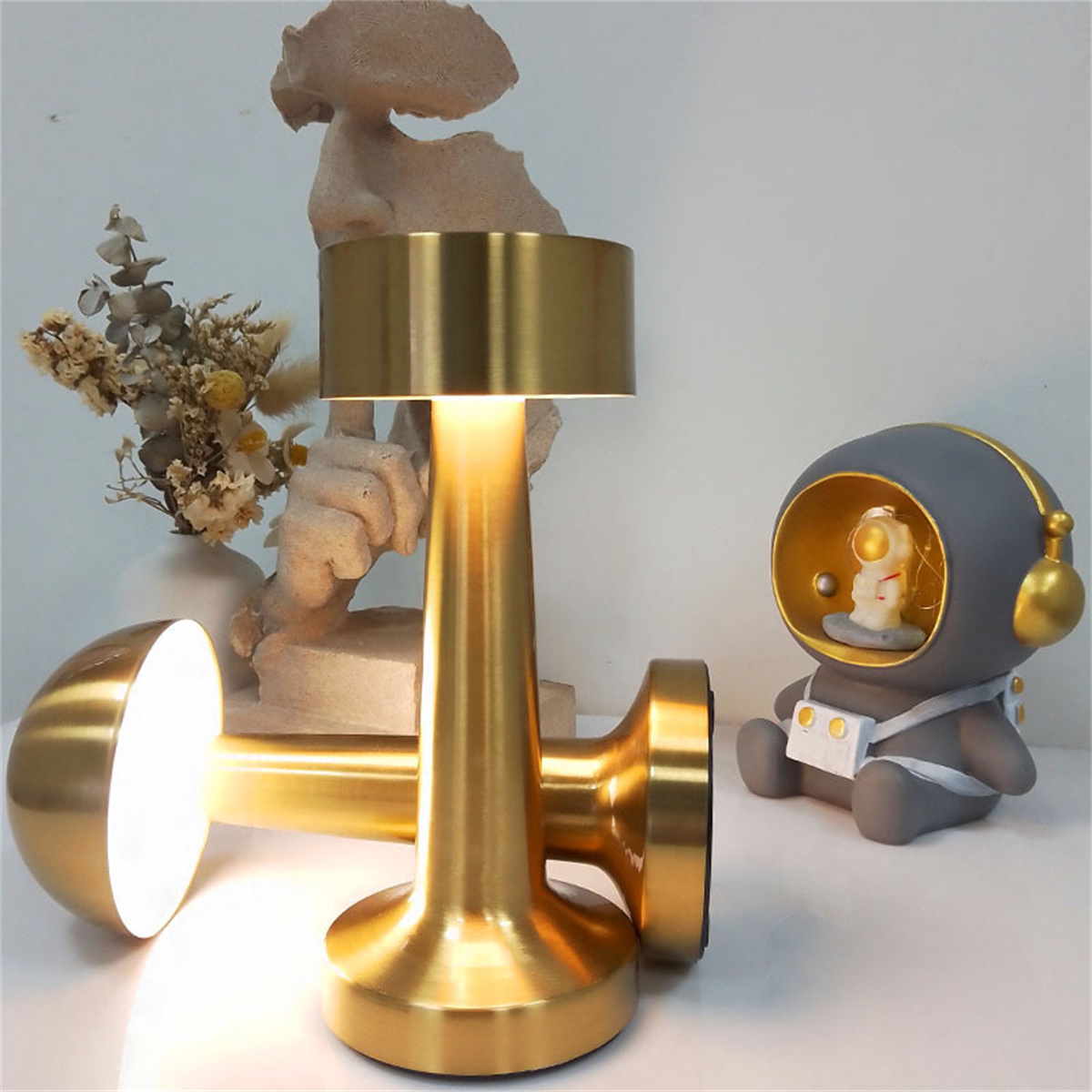 Goldene Lampen mit einem kleinen Astronautenspielzeug und einer Vase mit Trockenblumen.