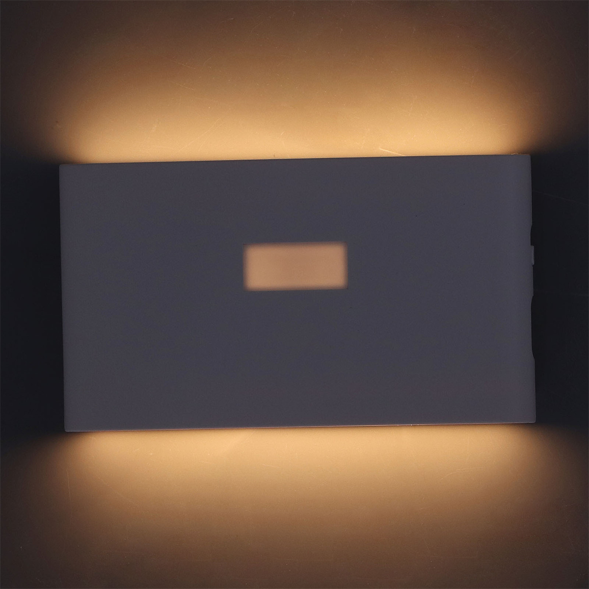 Eine Wandleuchte, die Licht auf dunklem Hintergrund ausstrahlt. Die Leuchte ist weiß.