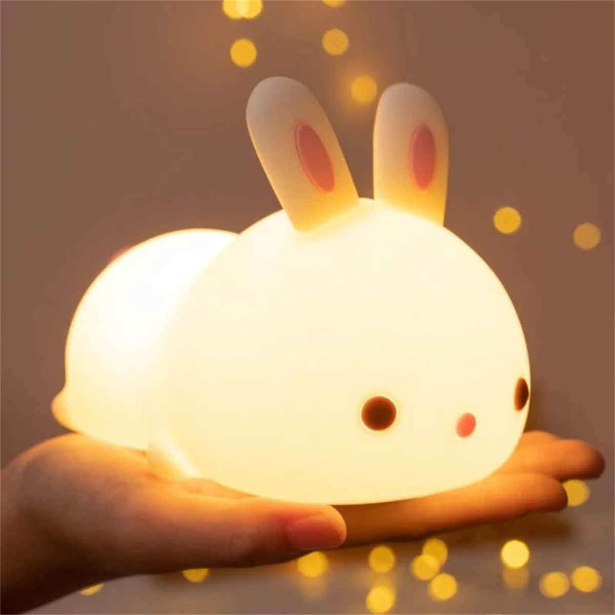 Ein weißes Hasen-Nachtlicht. Der Hase hat rosa Ohren und rote Augen und wird in einer Hand gehalten.