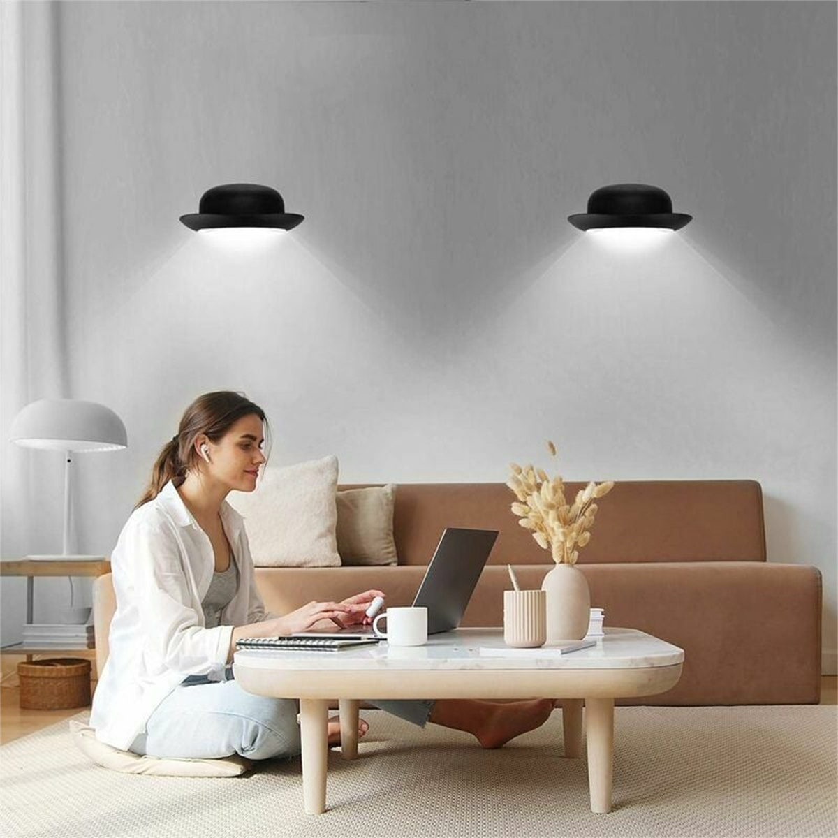 Frau arbeitet am Laptop, zwei Melonen-Hut-Leuchten an der Wand, braunes Sofa, Tisch.