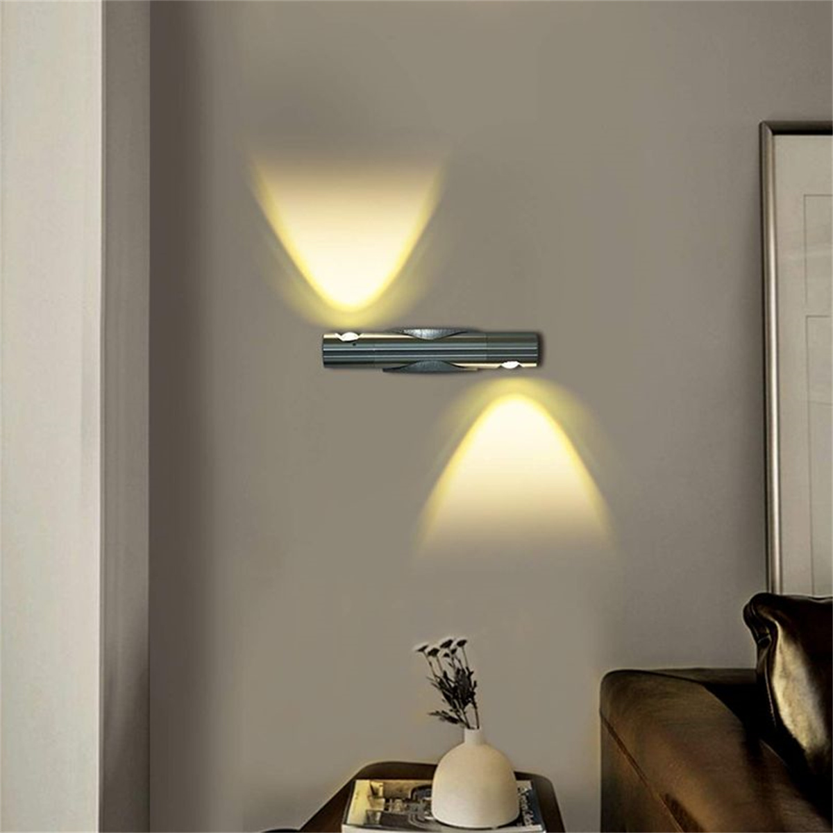 Eine silberne Wandlampe mit zwei nach unten gerichteten Lichtern an einer grauen Wand.