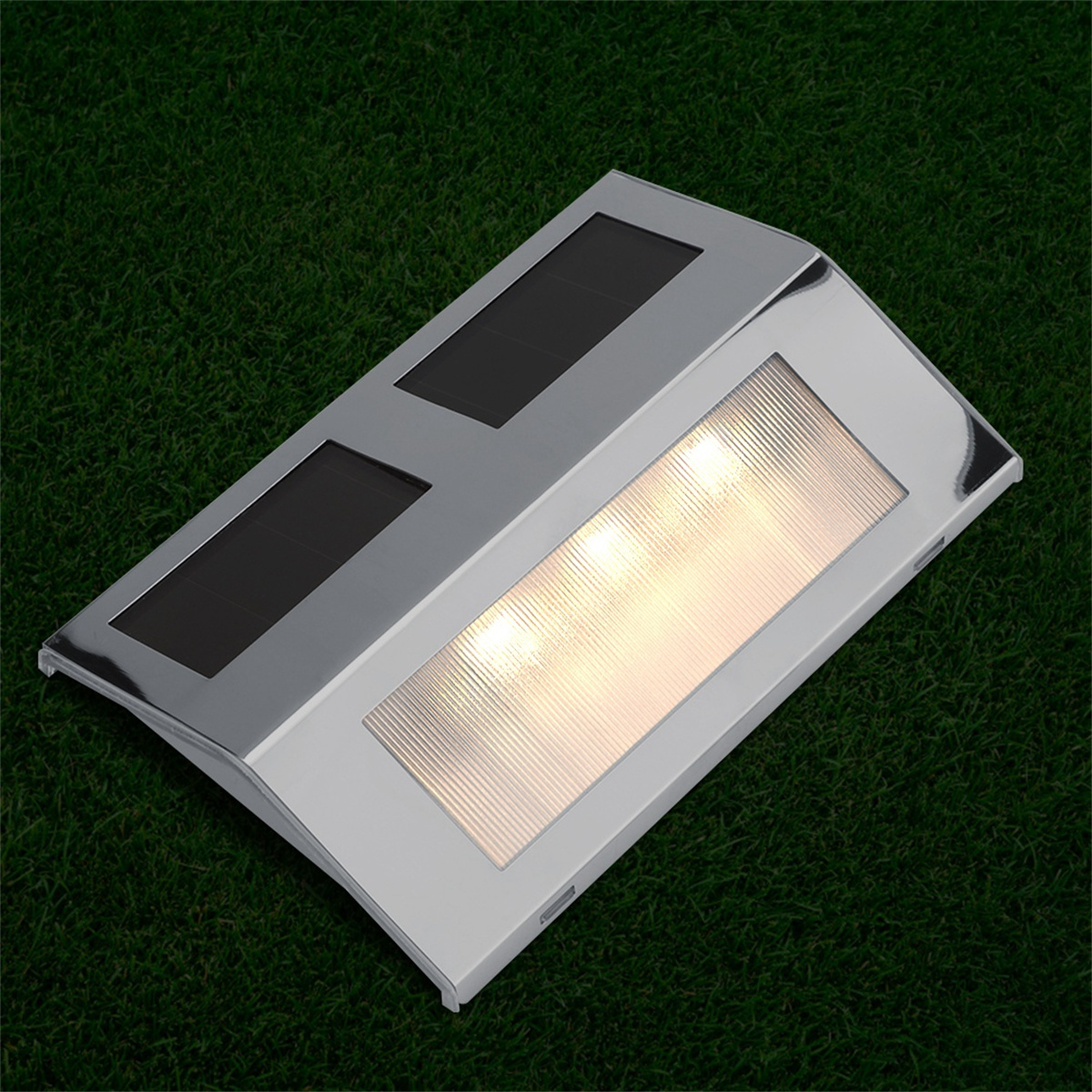 Eine silberne Außenleuchte auf einem grünen Rasen. Sie hat Solarpanels und ein Lichtpanel mit drei beleuchteten Lichtern.
