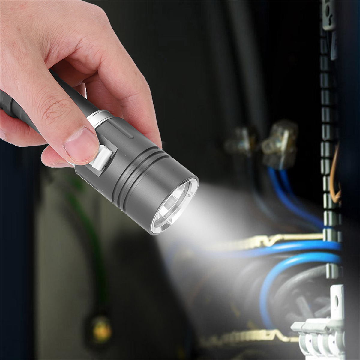 Hand hält graue Taschenlampe, leuchtet auf Drähte in dunkler Schalttafel.