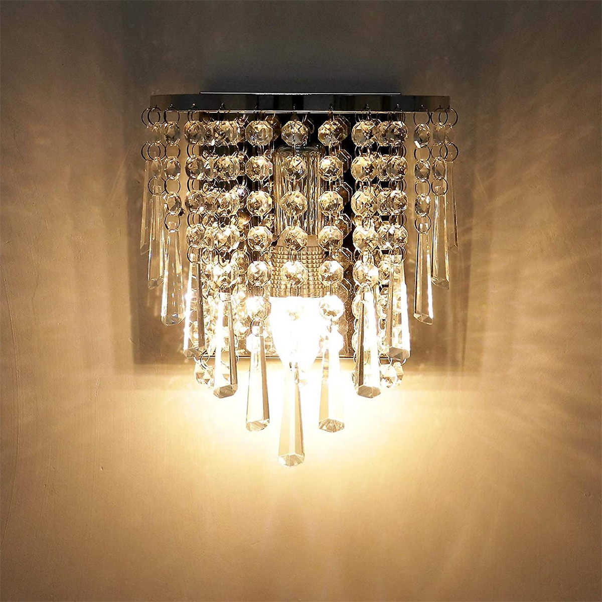 Eine dekorative Wandleuchte mit Kristallen, die von einem silbernen Rahmen hängen, beleuchtet von warmem Licht.