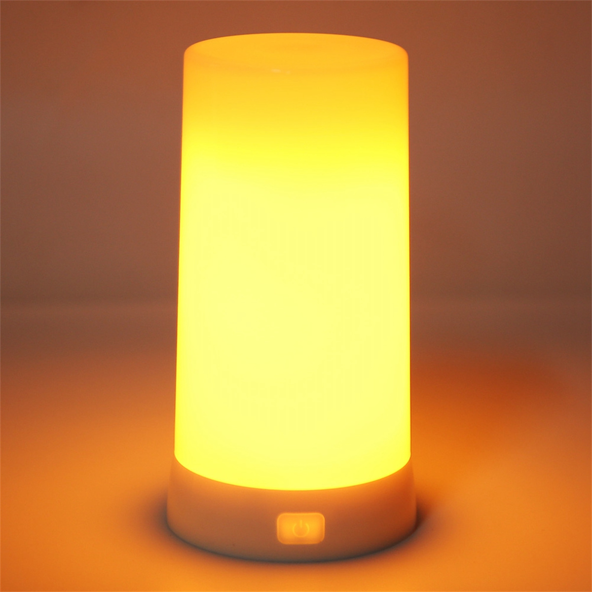 Eine zylindrische Lampe, die orange leuchtet, auf einer braunen Oberfläche. Die Lampe ist an.
