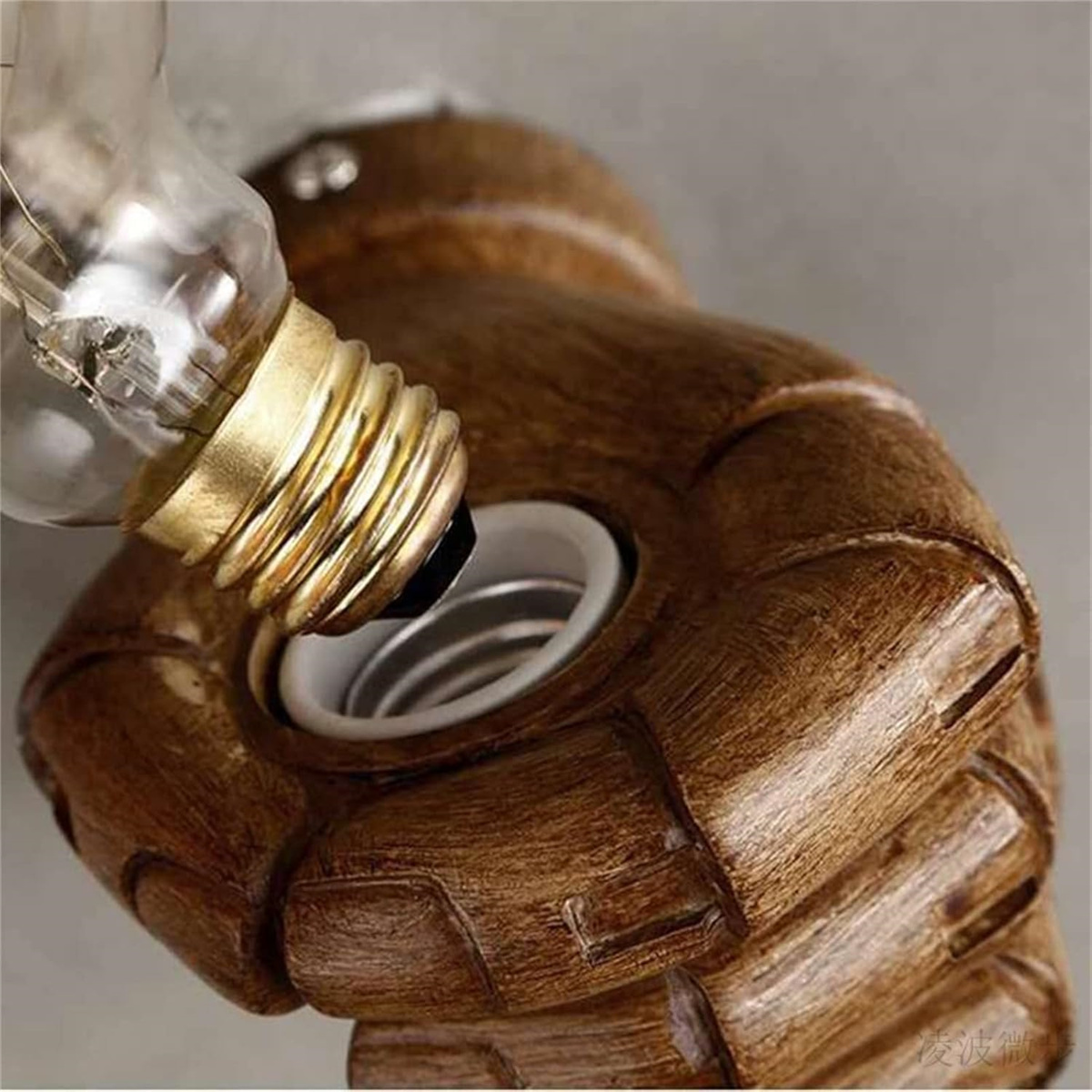 Ein brauner, faustförmiger Lampenhalter hält eine Glühbirne mit goldenem Sockel.