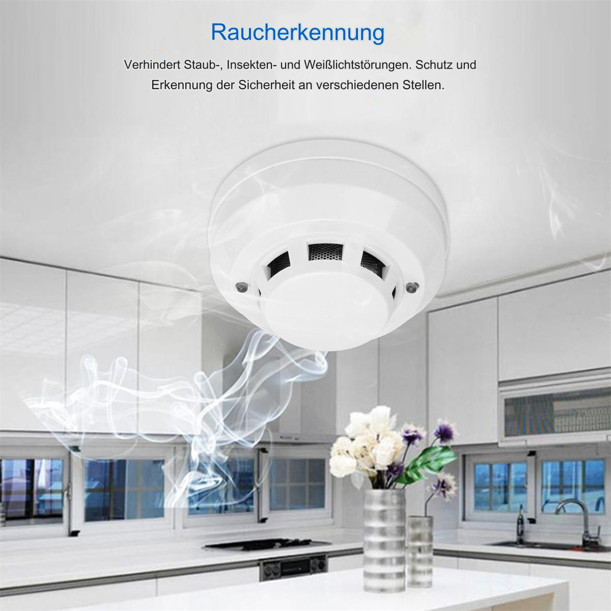 Ein Rauchmelder an einer Decke, mit Rauch und Küche im Hintergrund.