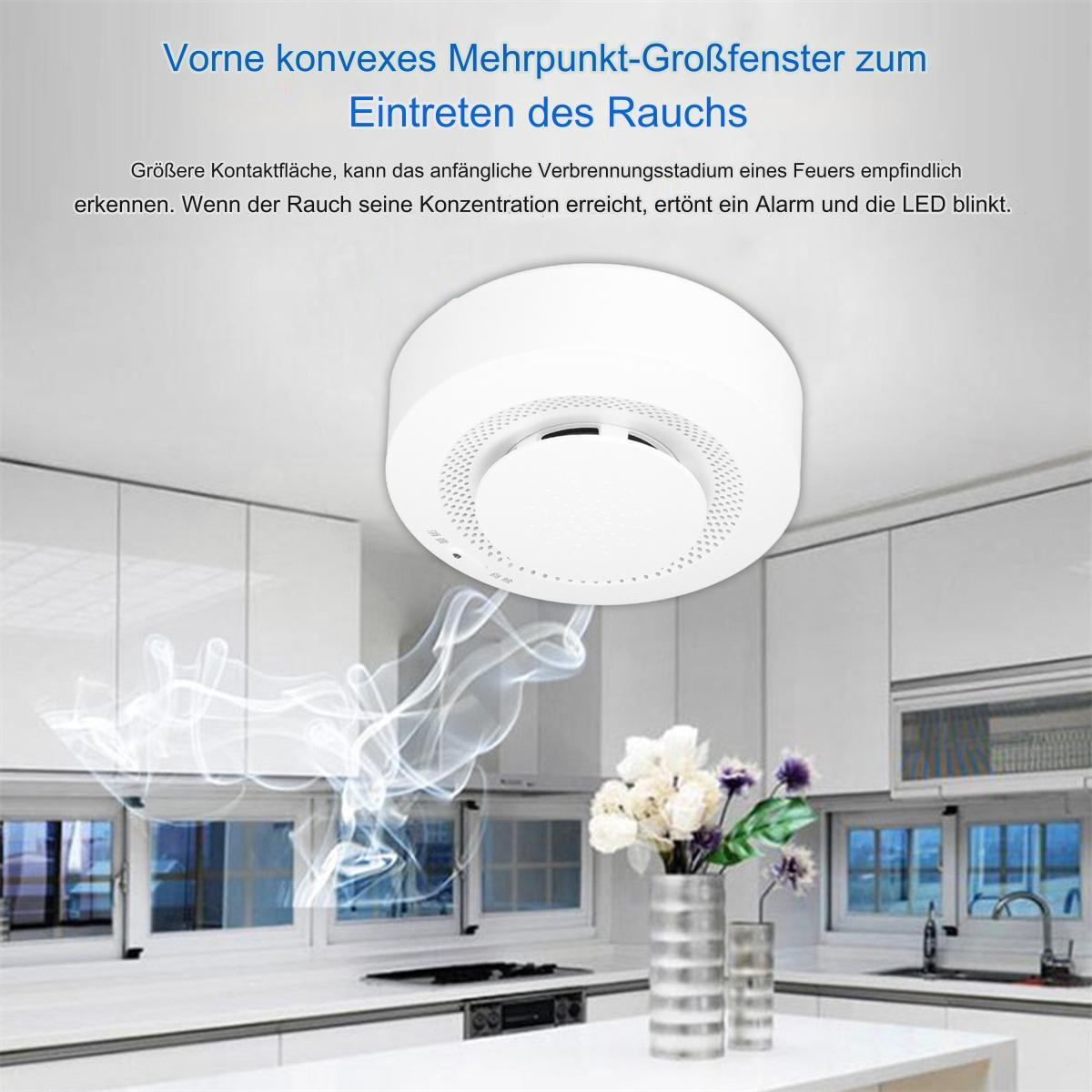 Ein Rauchmelder an einer weißen Decke. Eine Vase mit Blumen steht auf dem Tisch darunter.
