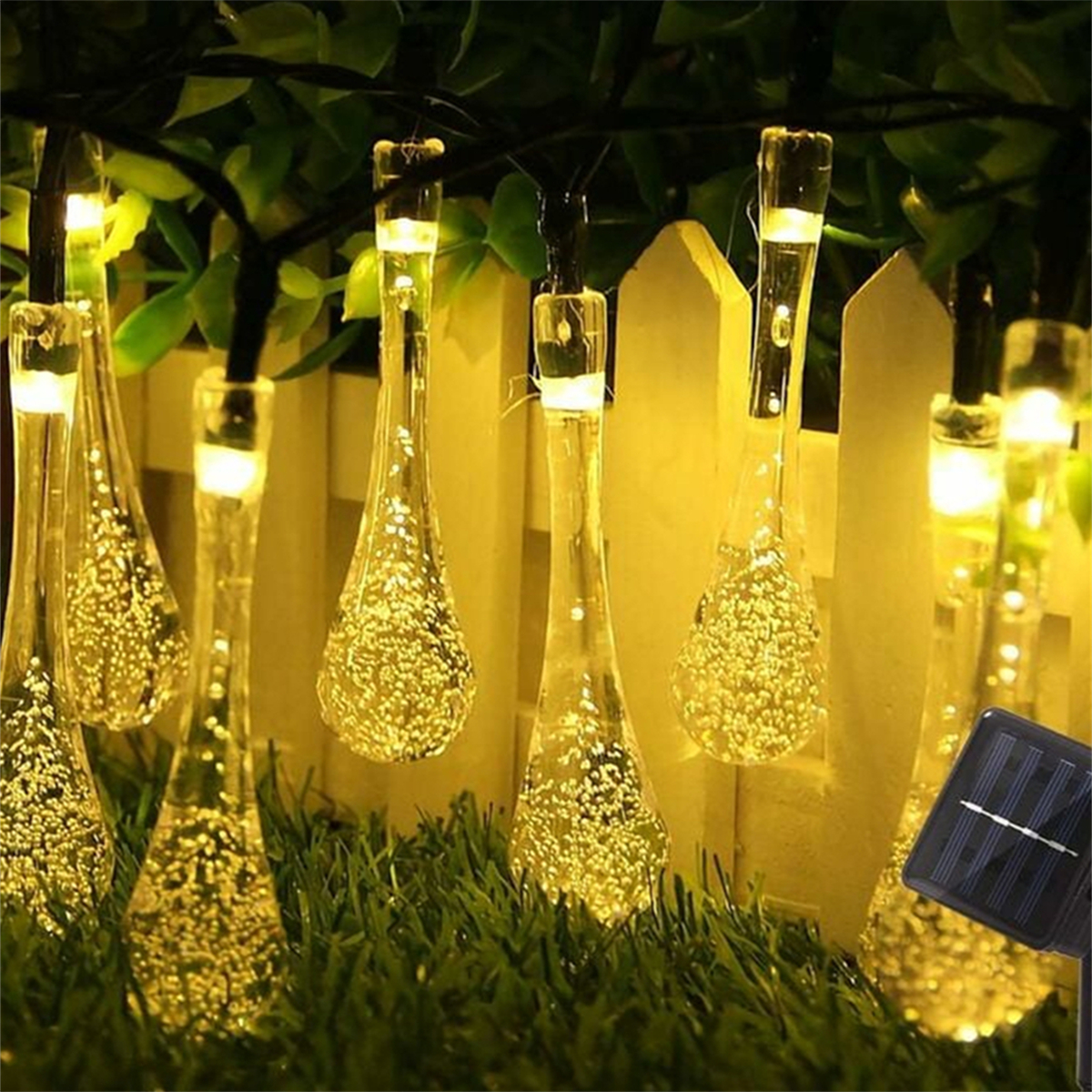 Lichterkette mit tropfenförmigen Lichtern, die über grünem Gras und einem Zaun hängen.