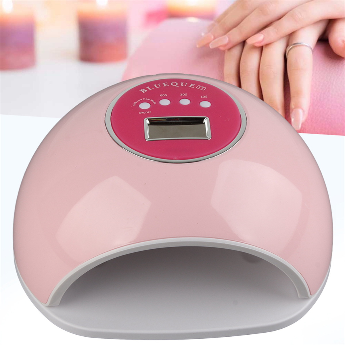 Ein rosa Nageltrockner mit Digitalanzeige und im Hintergrund Hände einer Frau mit Ring.
