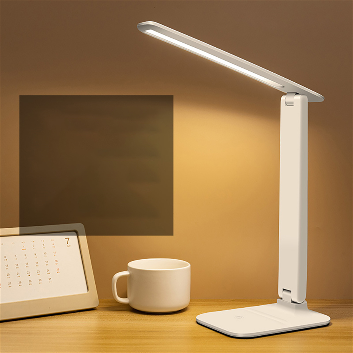 Weiße Schreibtischlampe mit langem Lichtbalken auf einem Holztisch. Ein Kalender und eine Tasse liegen daneben.