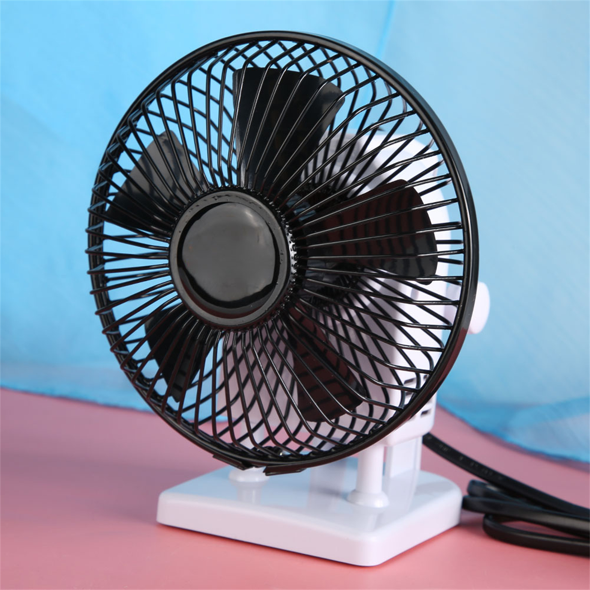 Ein kleiner, weißer Schreibtischventilator mit schwarzen Flügeln und einem schwarzen Schutzgitter. Er steht auf einer rosa Oberfläche.