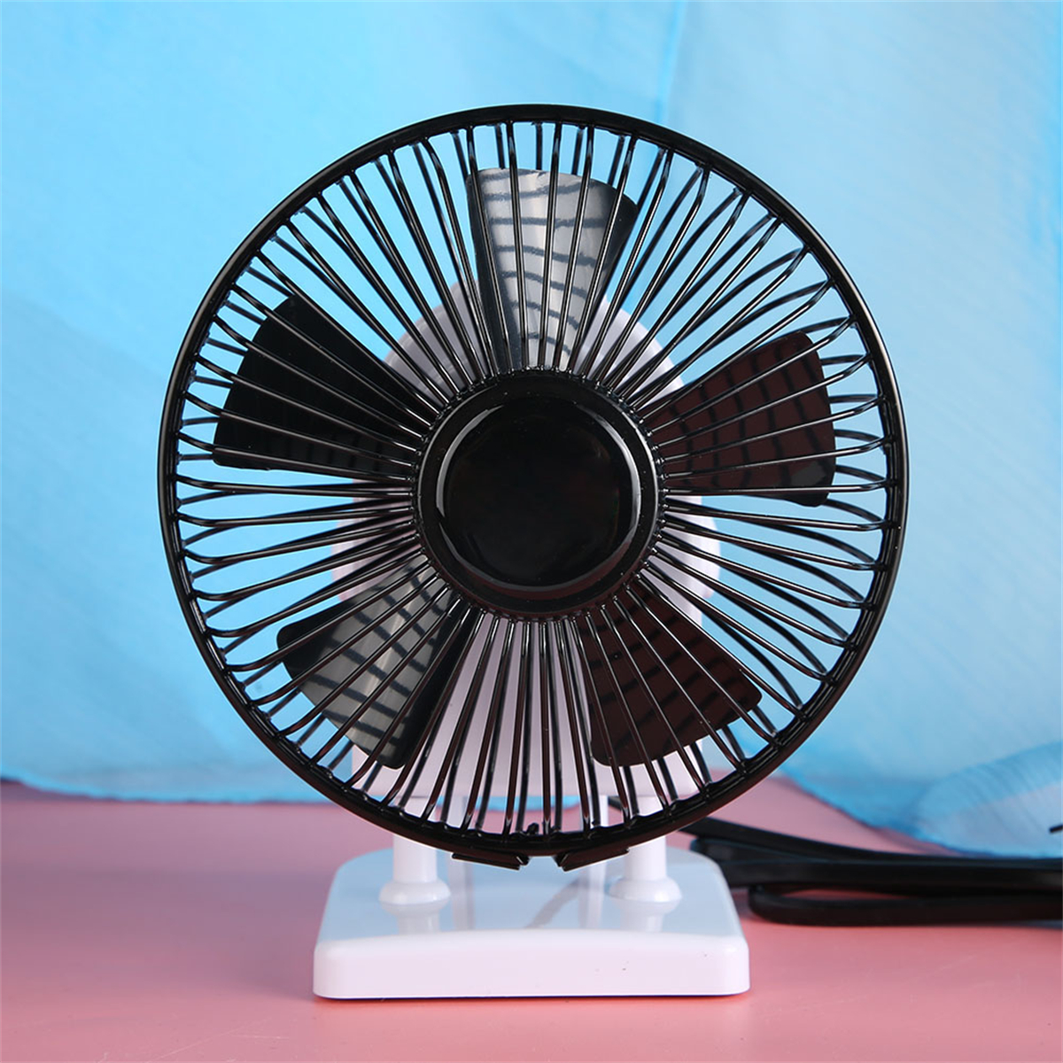 Ein schwarzer Schreibtischventilator mit weißem Sockel und rundem Käfig, die Rotorblätter sind sichtbar.