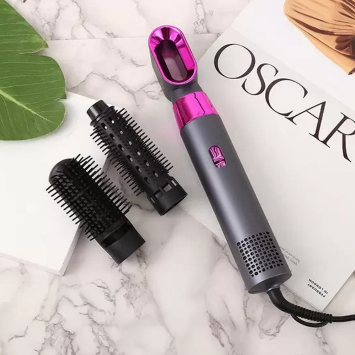 Haarstyling-Werkzeug mit mehreren Bürstenköpfen. Das Werkzeug ist grau und rosa, die Bürstenköpfe sind schwarz.