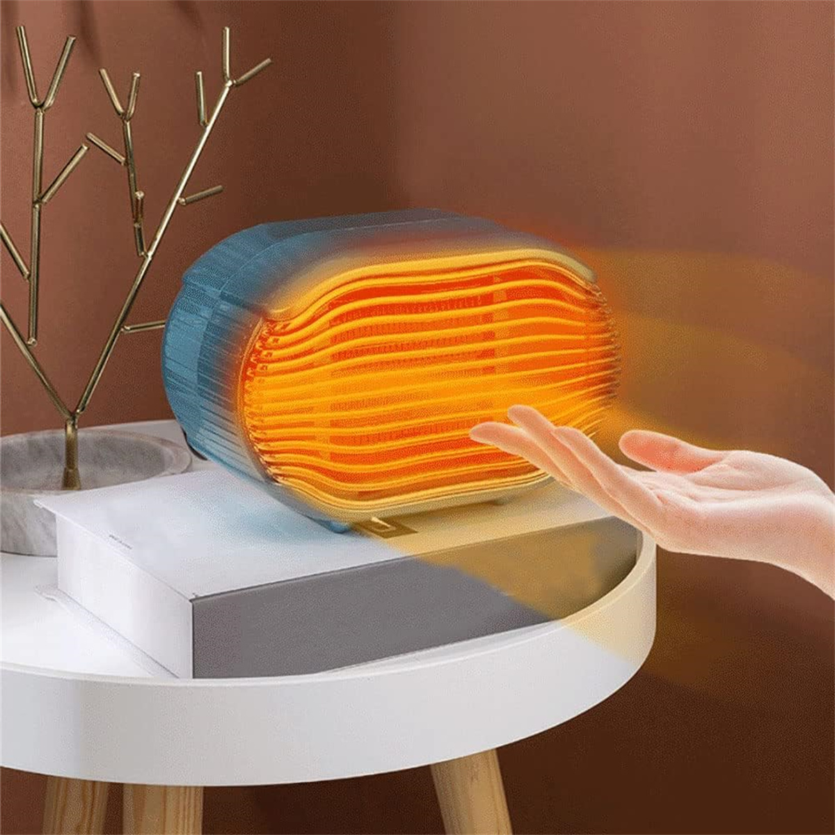 Ein kleiner elektrischer Heizlüfter. Eine Hand greift danach. Eine kleine Pflanze im Hintergrund.