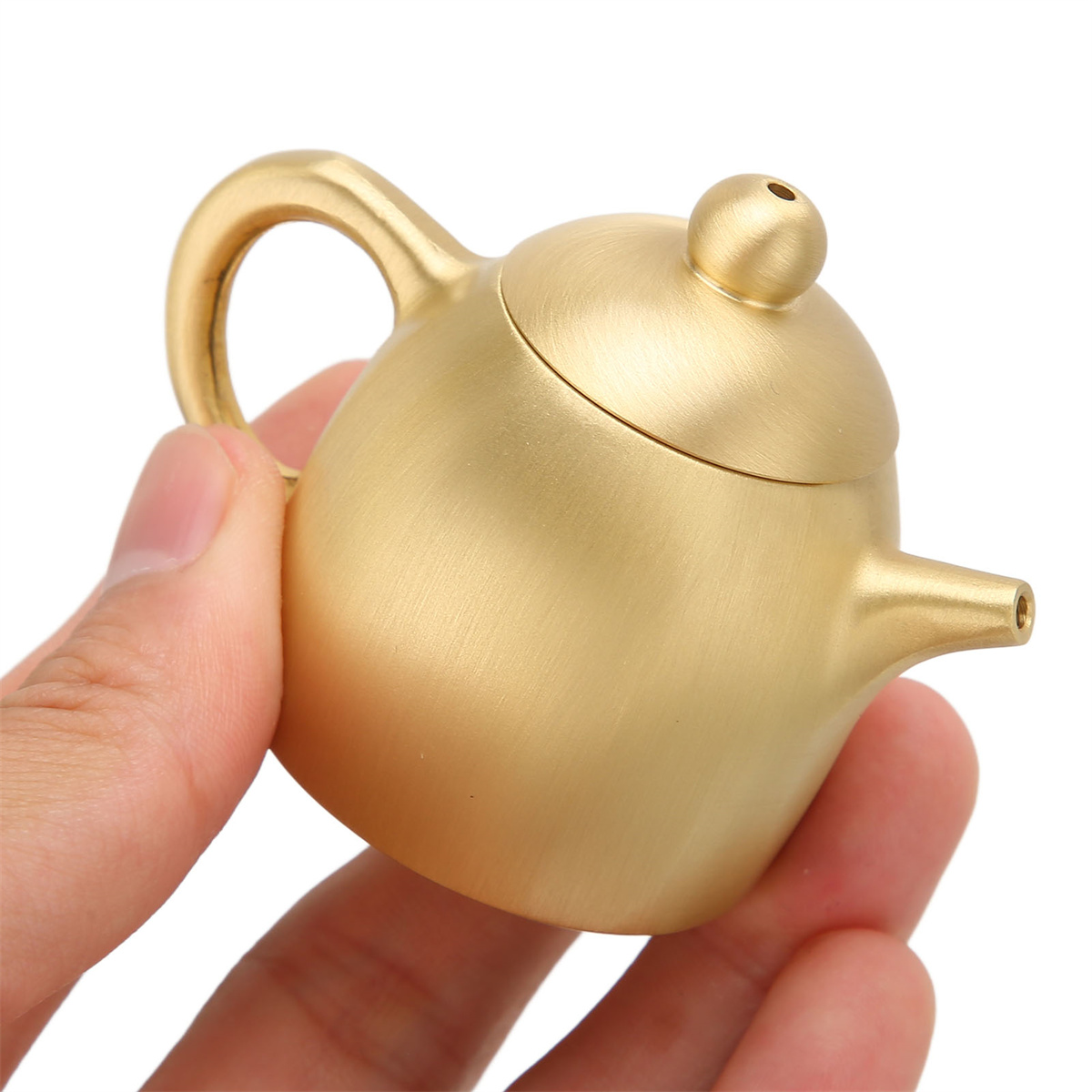 Kleine, goldene Teekanne in der Hand gehalten. Sie hat einen Griff, Ausguss, Deckel und Knauf.