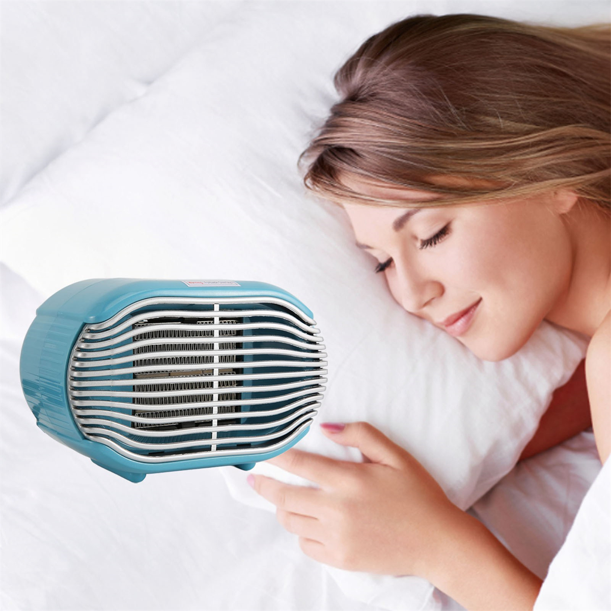 Schlafende Frau neben einem blau-weißen elektrischen Heizgerät auf einem weißen Bett, in einem Schlafzimmer.