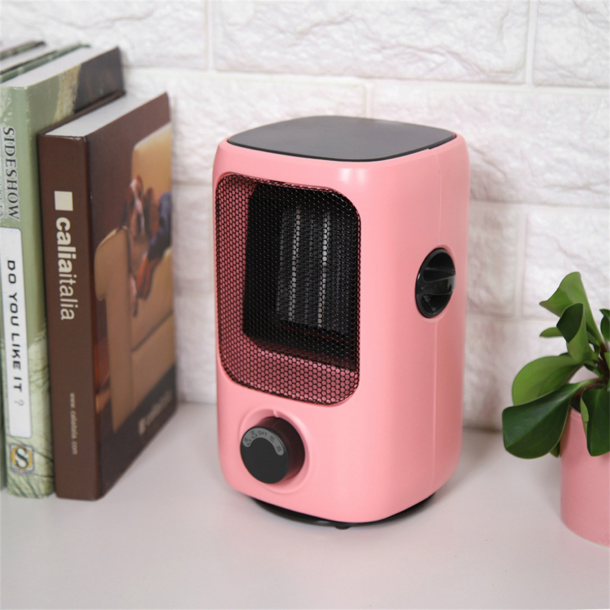 Rosa Mini-Heizung auf weißem Tisch. Bücher links, eine Pflanze rechts.