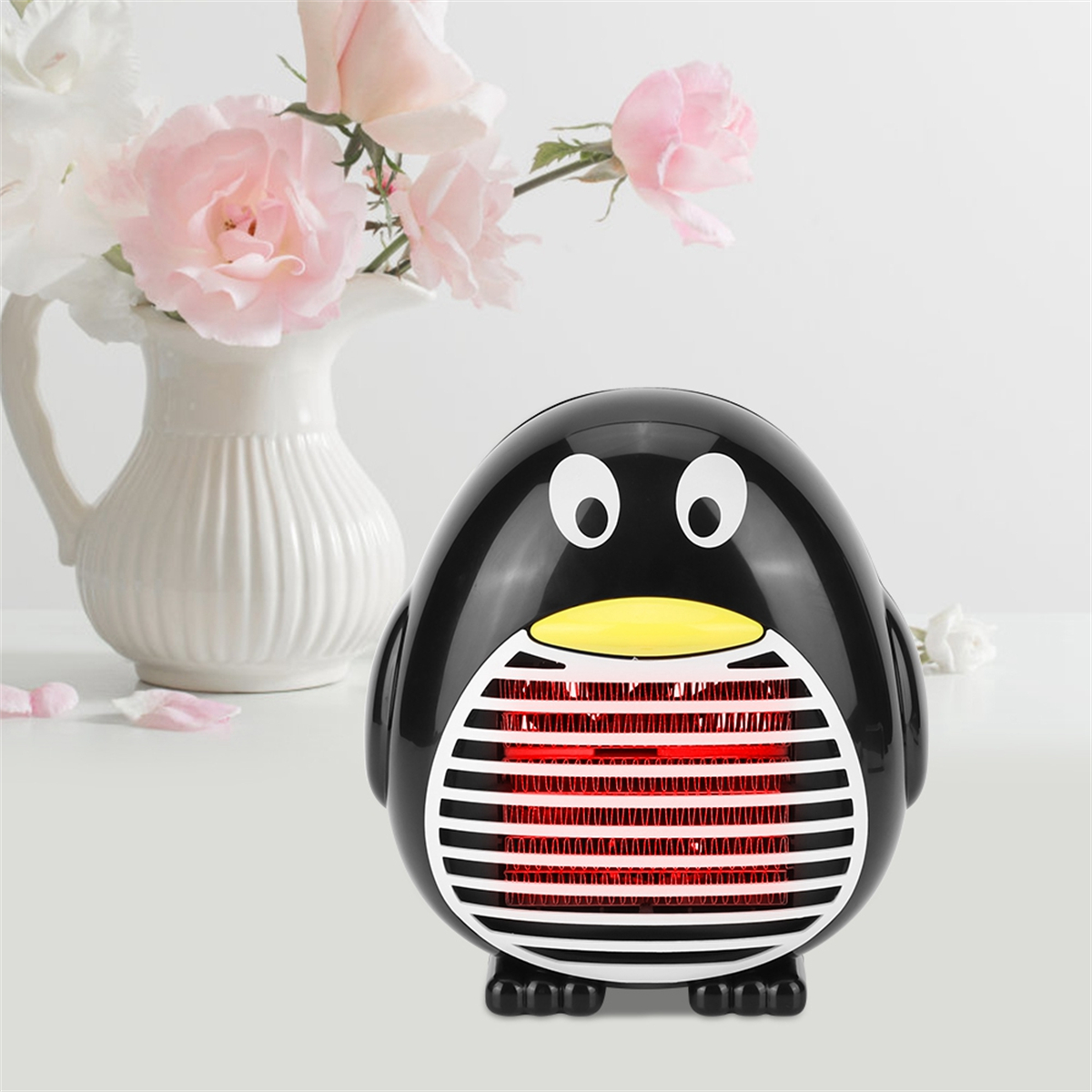 Ein pinguinförmiger Heizlüfter mit rotem Heizelement, vor Blumen in einer Vase. Weiße Oberfläche.