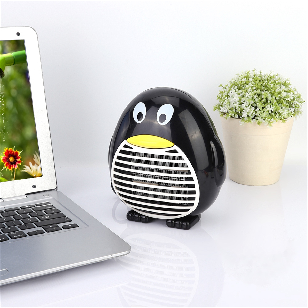 Ein schwarzer Pinguin-Heizkörper auf einem Tisch. Ein Laptop und eine kleine Topfpflanze sind in der Nähe.